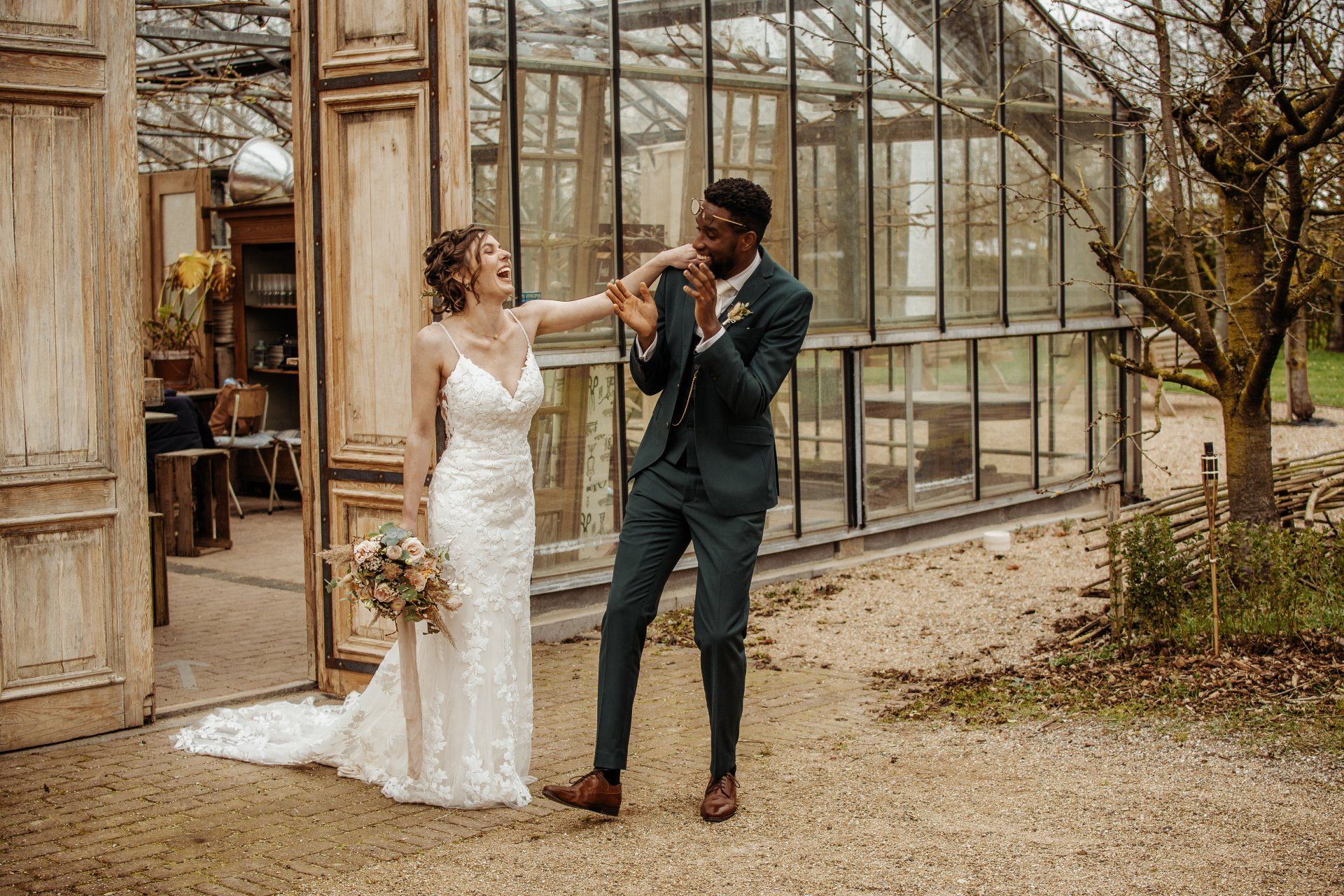 Een bruid en bruidegom staan naast elkaar voor een kas.