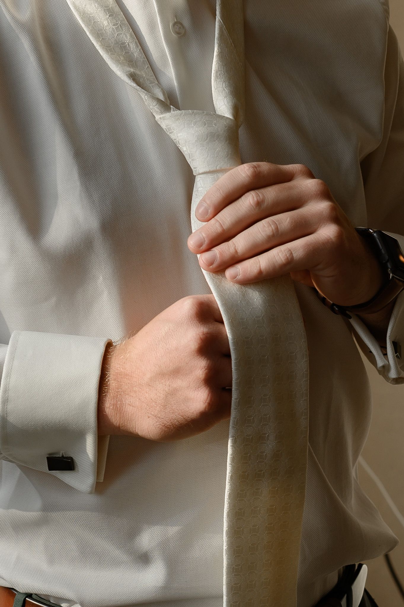 Een bruidegom in een wit overhemd knoopt zijn stropdas vast