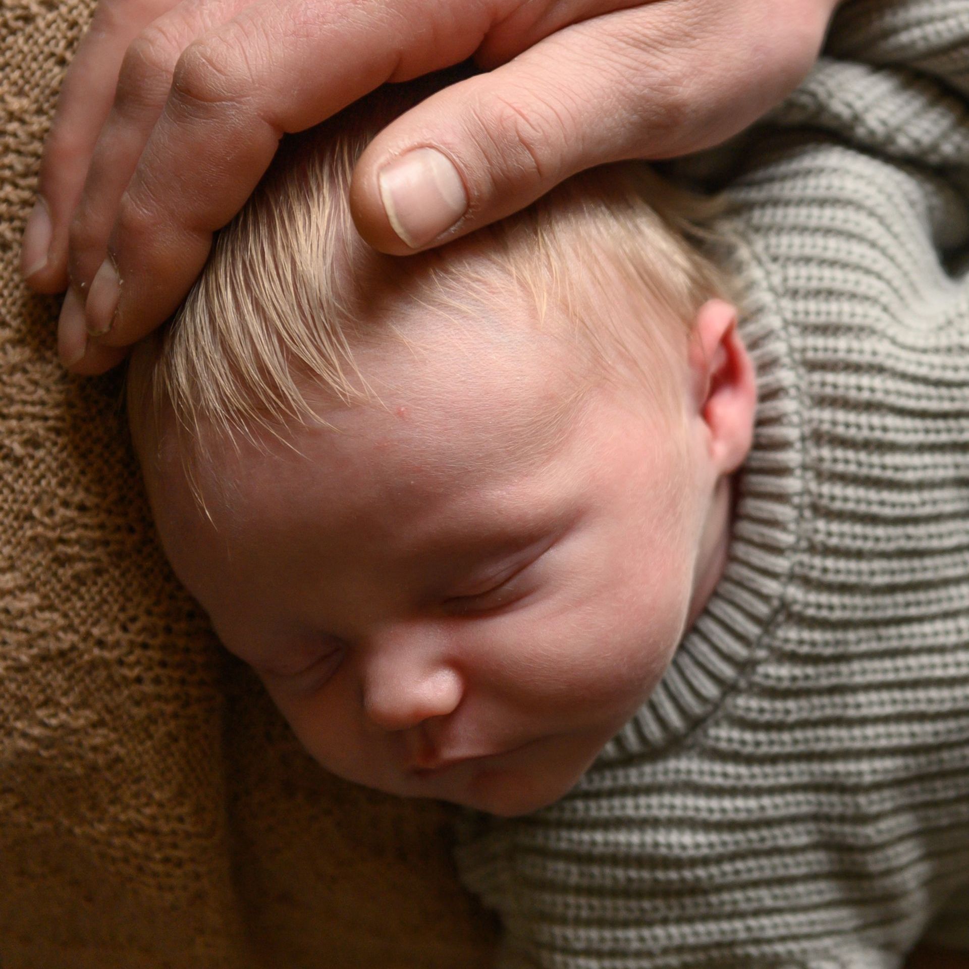 Een slapende baby met blond haar wordt zachtjes over het hoofdje geaaid.