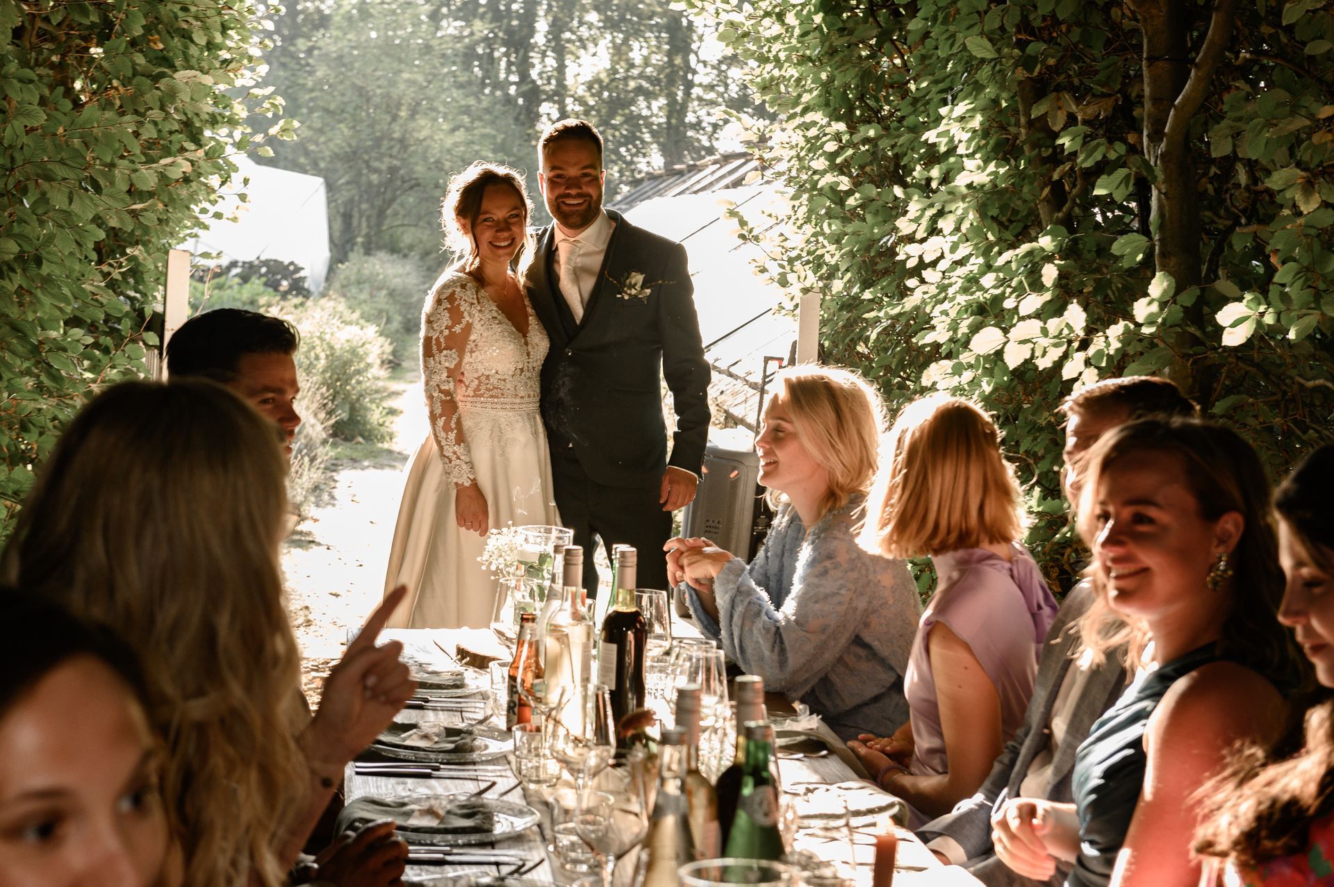 Een bruid en bruidegom staan met hun bruiloftsgasten voor een lange tafel.
