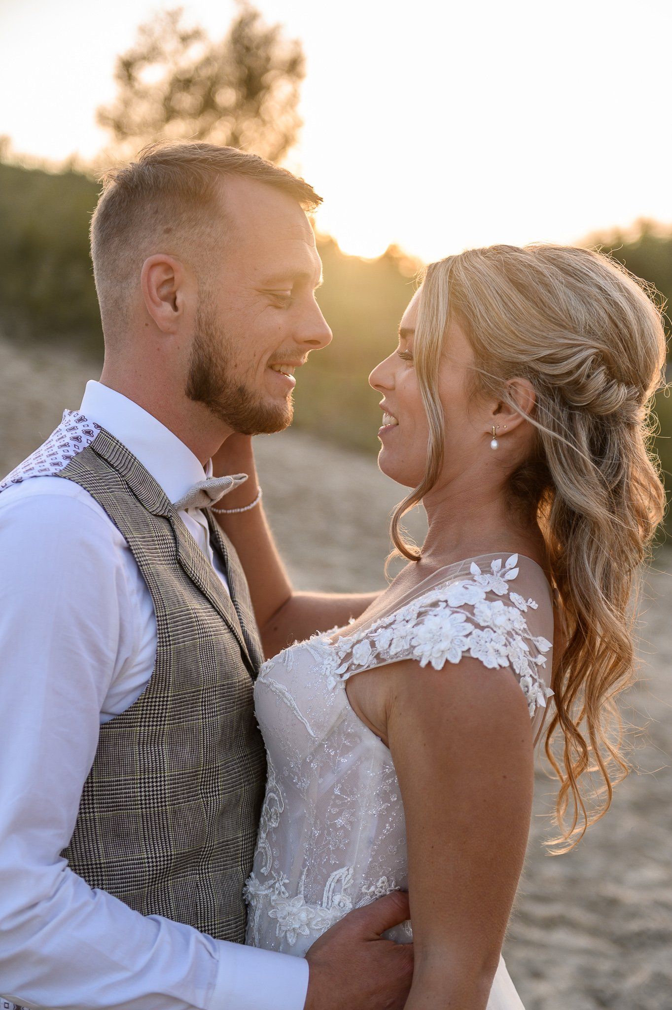 Een bruid en bruidegom kijken elkaar in de ogen op het strand.