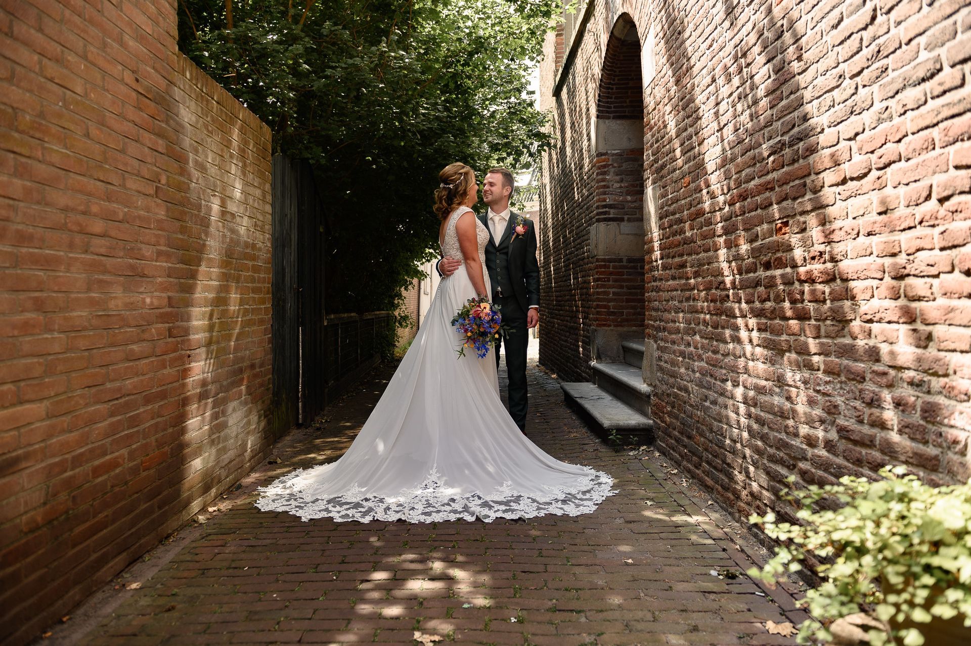 Een bruid en bruidegom staan naast elkaar in een smal steegje.