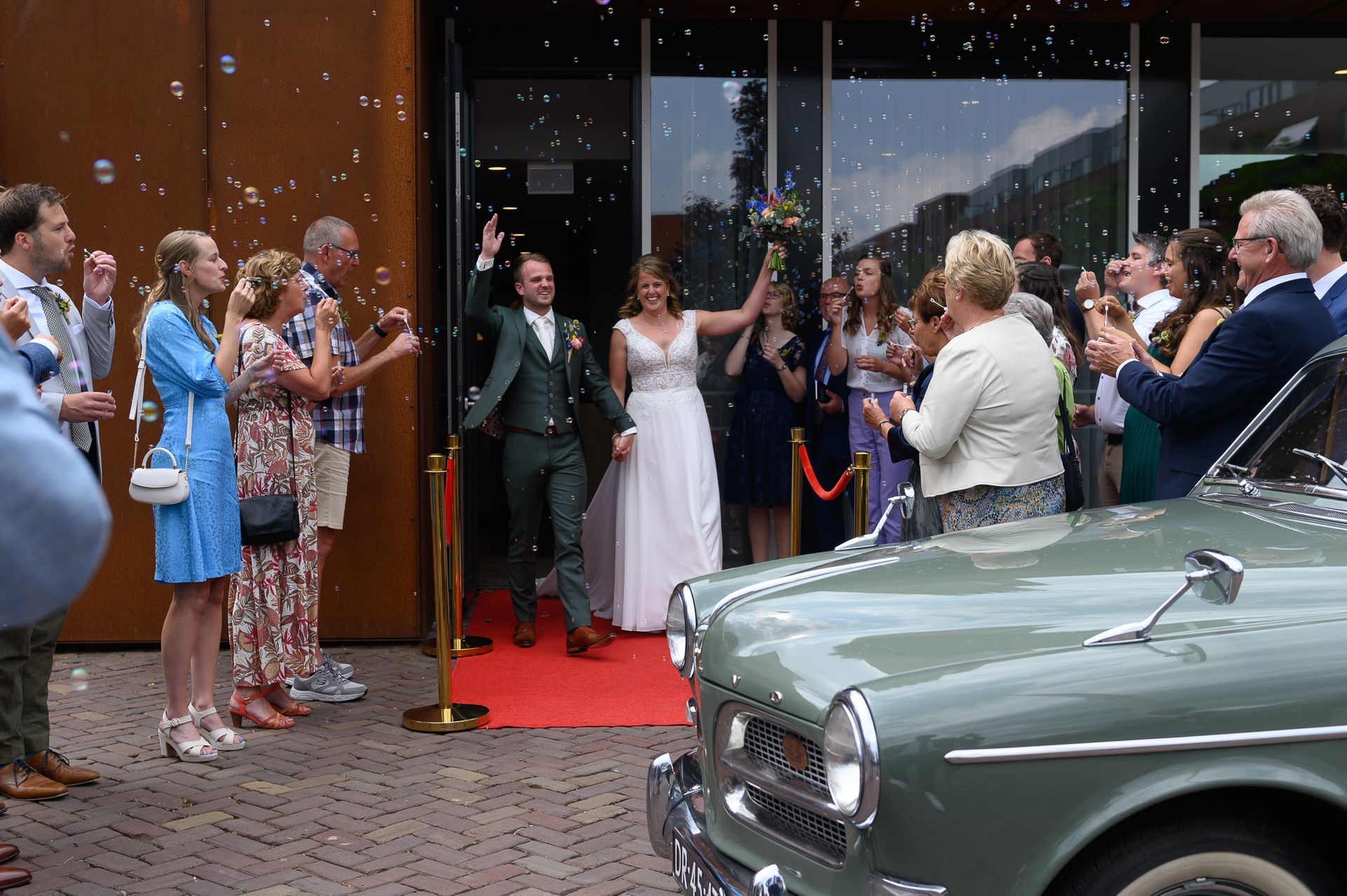 Een bruid en bruidegom komen uit het gemeentehuis terwijl een groep mensen bellen blazen.