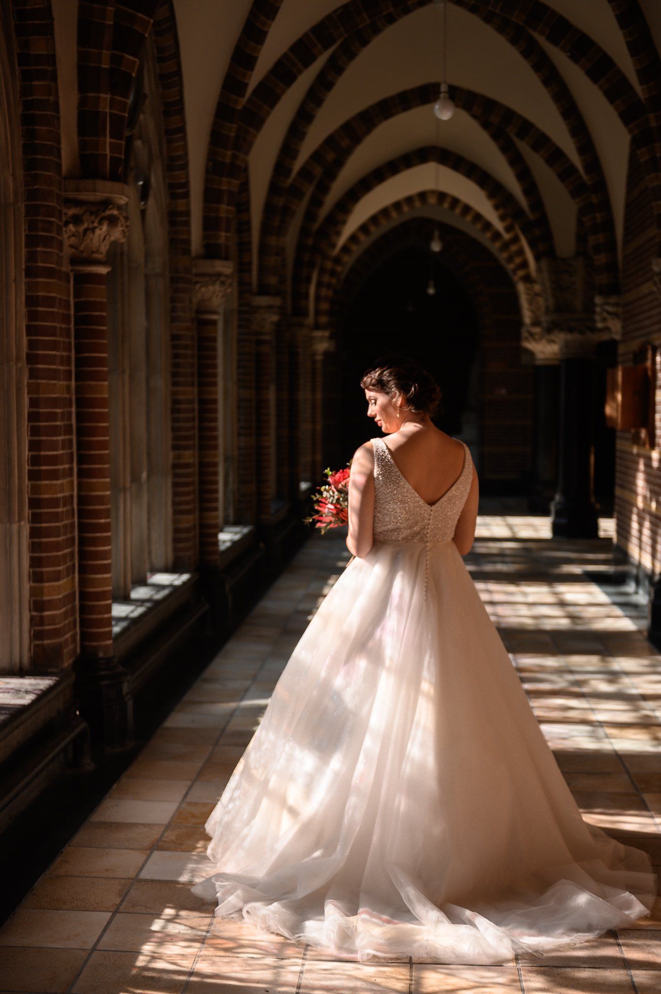 Een vrouw in een trouwjurk staat in een gang.