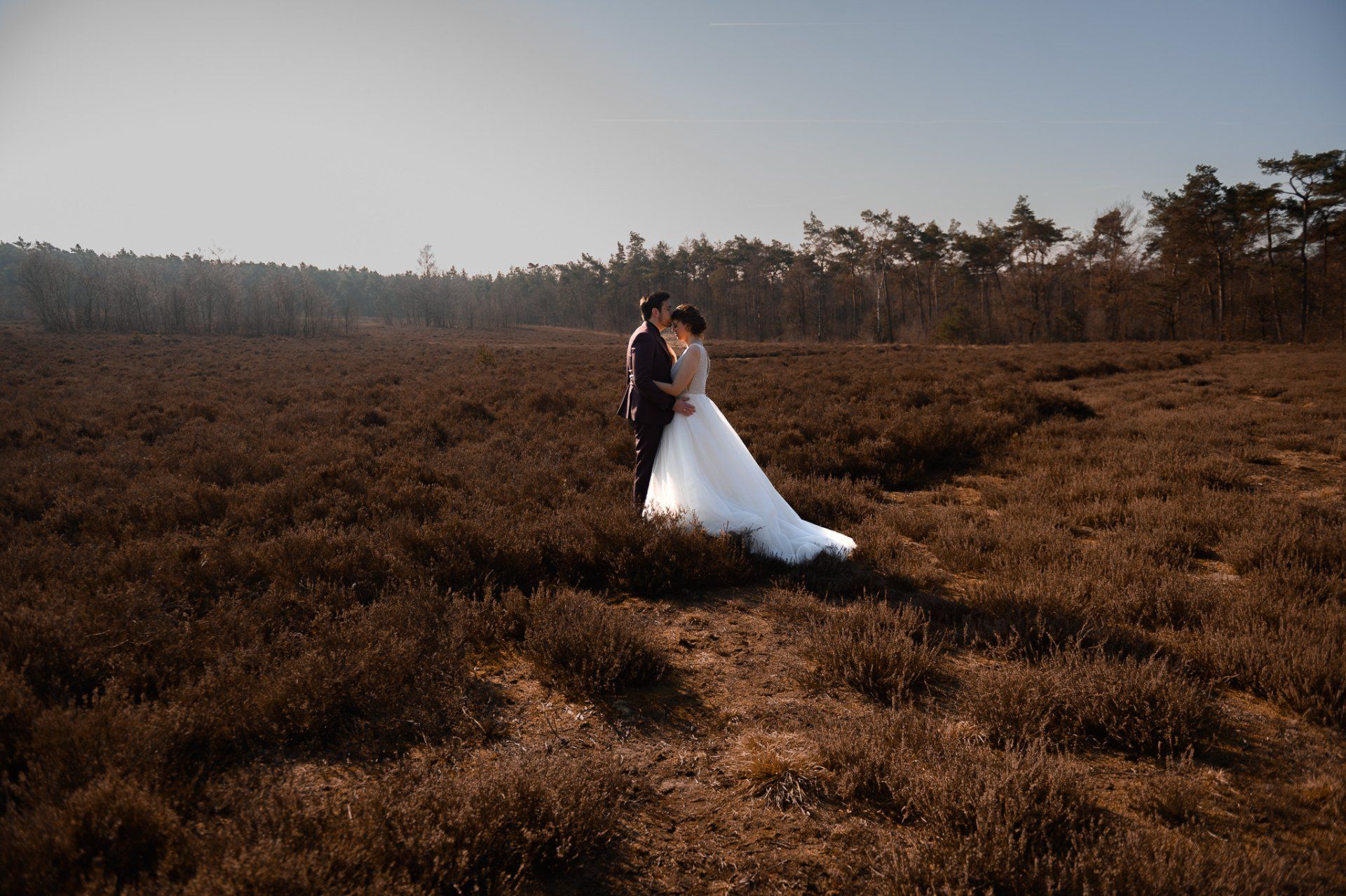 Een bruid en bruidegom staan in een veld.
