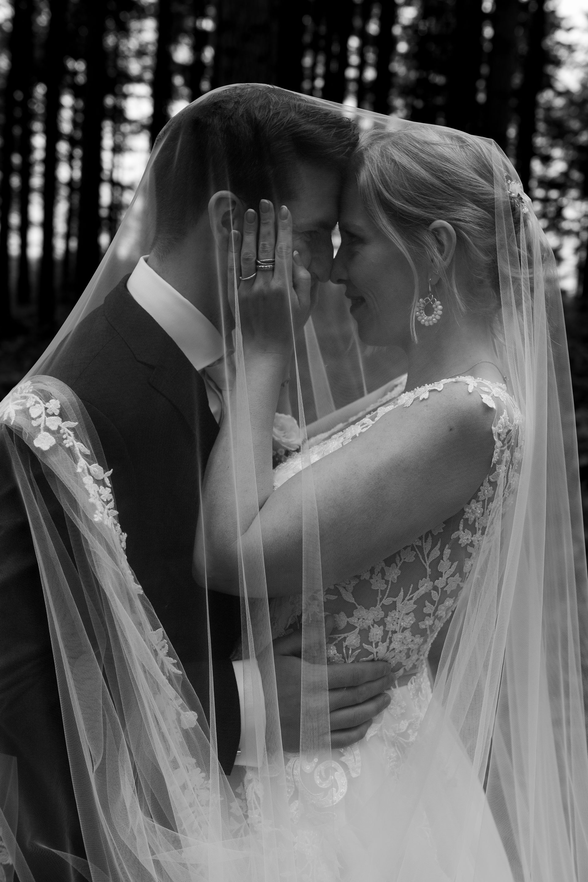 Op een zwart-witfoto kussen een bruid en bruidegom elkaar achter een sluier.