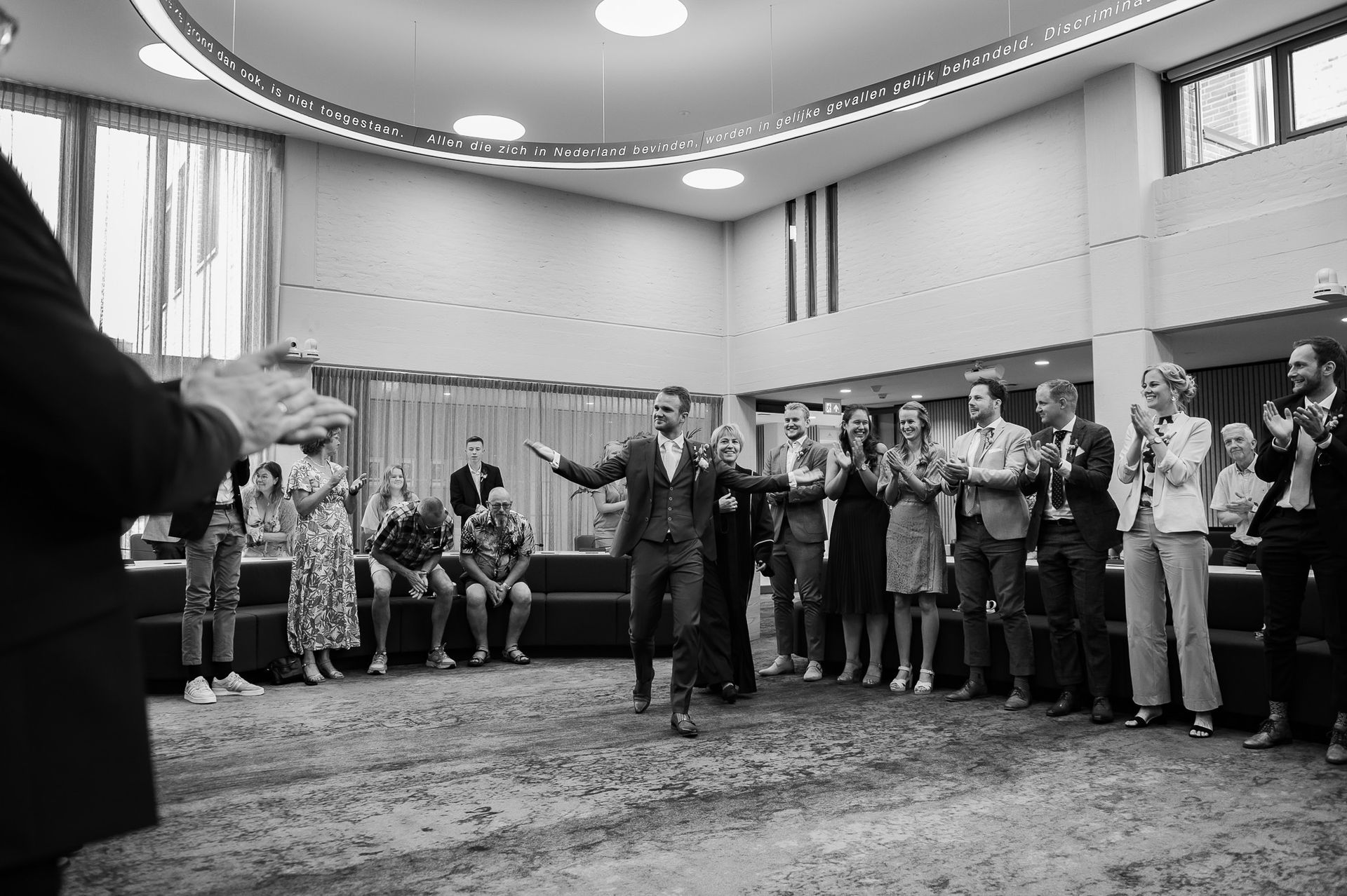 Een zwart-witfoto van een groep mensen en de bruidegom die binnen komt..