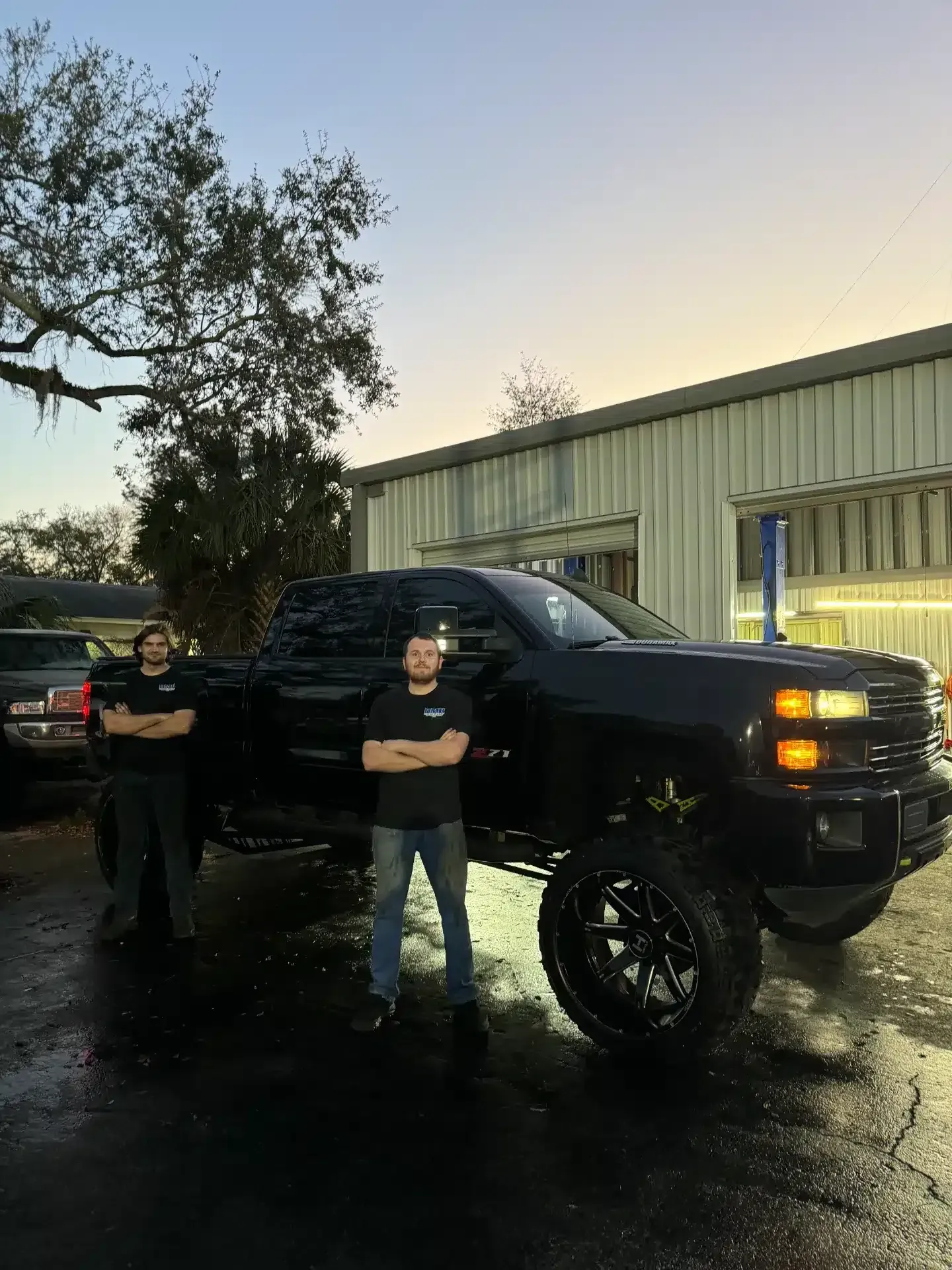 Black Truck parked outside during sunset, two staff members standing in front | DMR Diesel Repair, Inc
