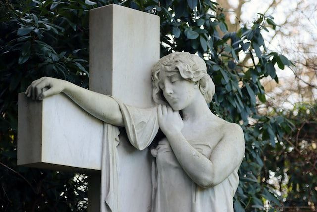 Stone angel statue resting beside a cross in a cemetery, symbolizing remembrance, faith, and honorin