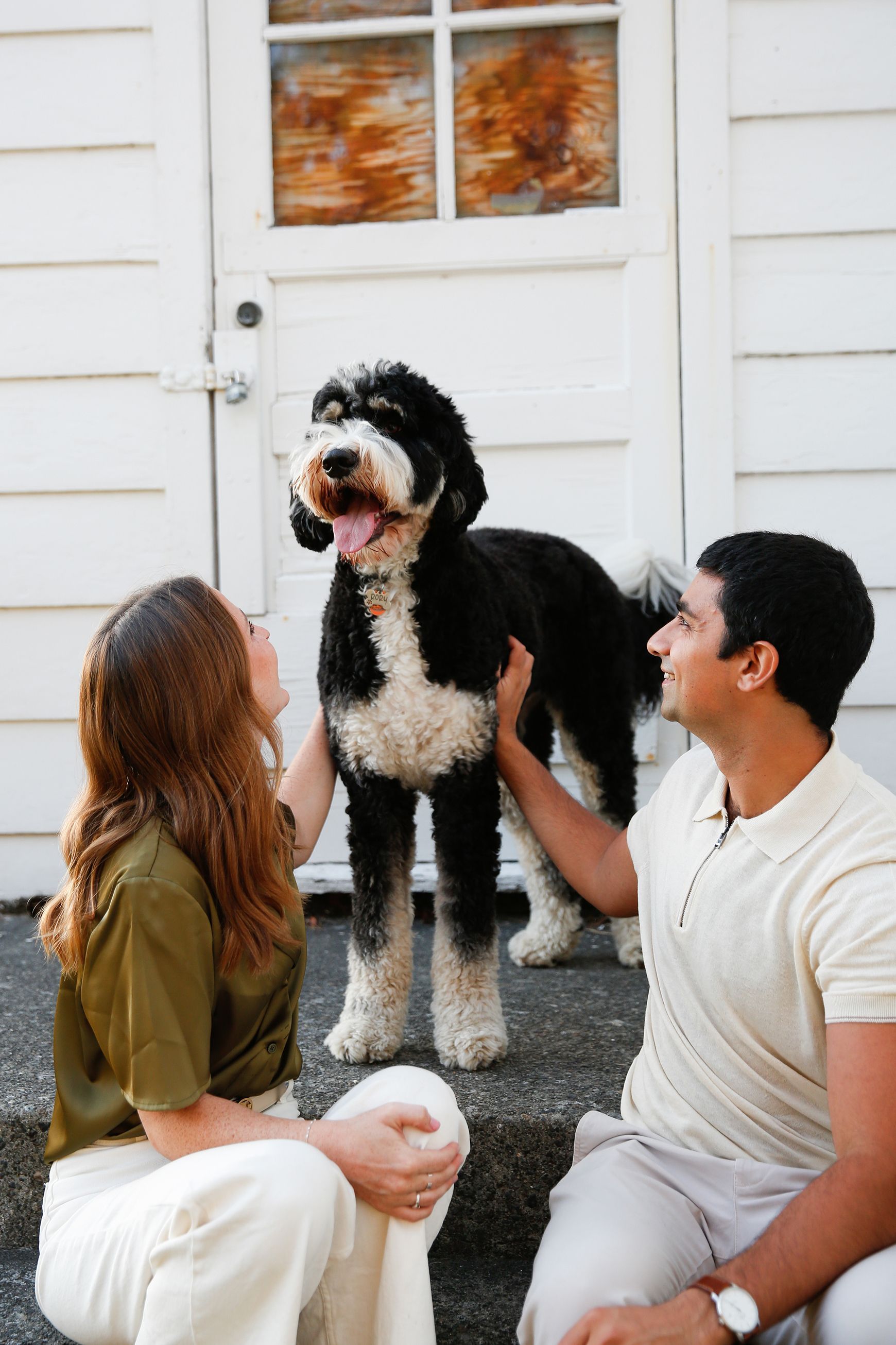 A man and a woman are petting a black and white dog.
