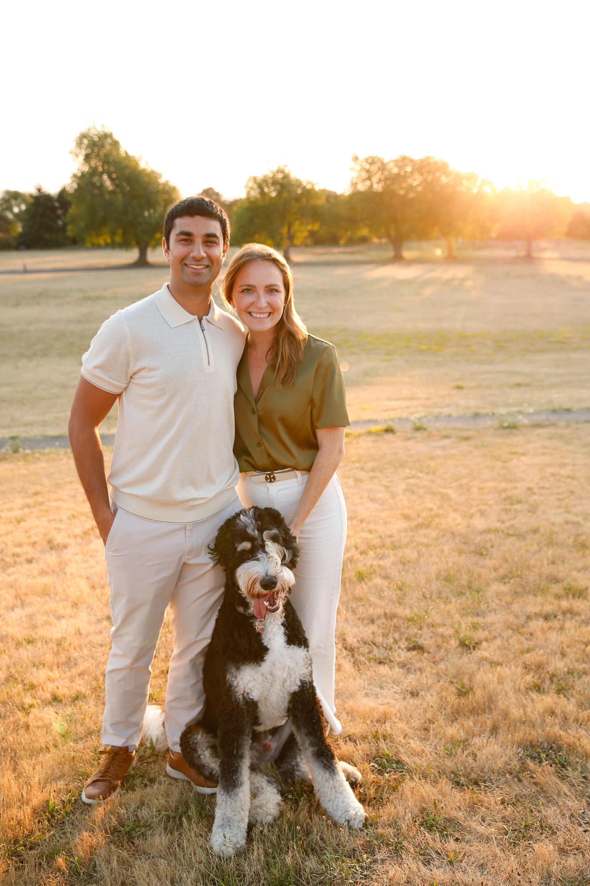 A man and a woman are standing next to a dog in a field.