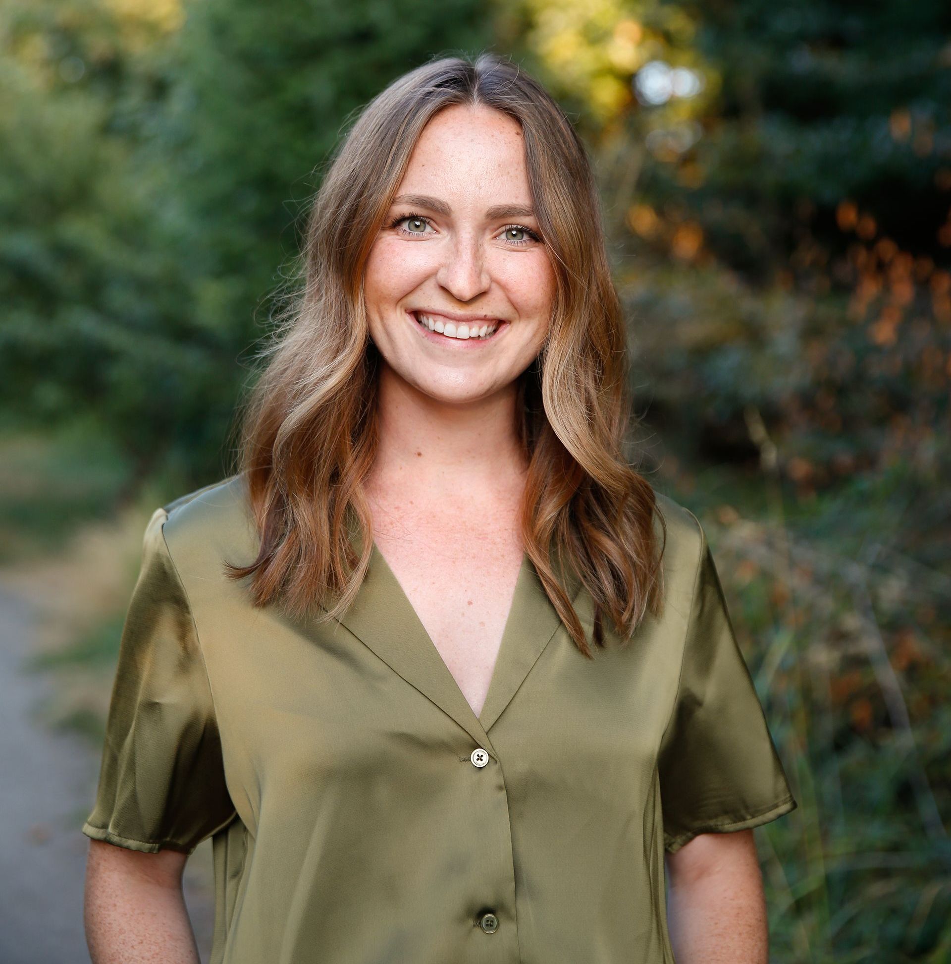 Dr. Annie in a black jacket is standing in front of a bush of pink flowers.