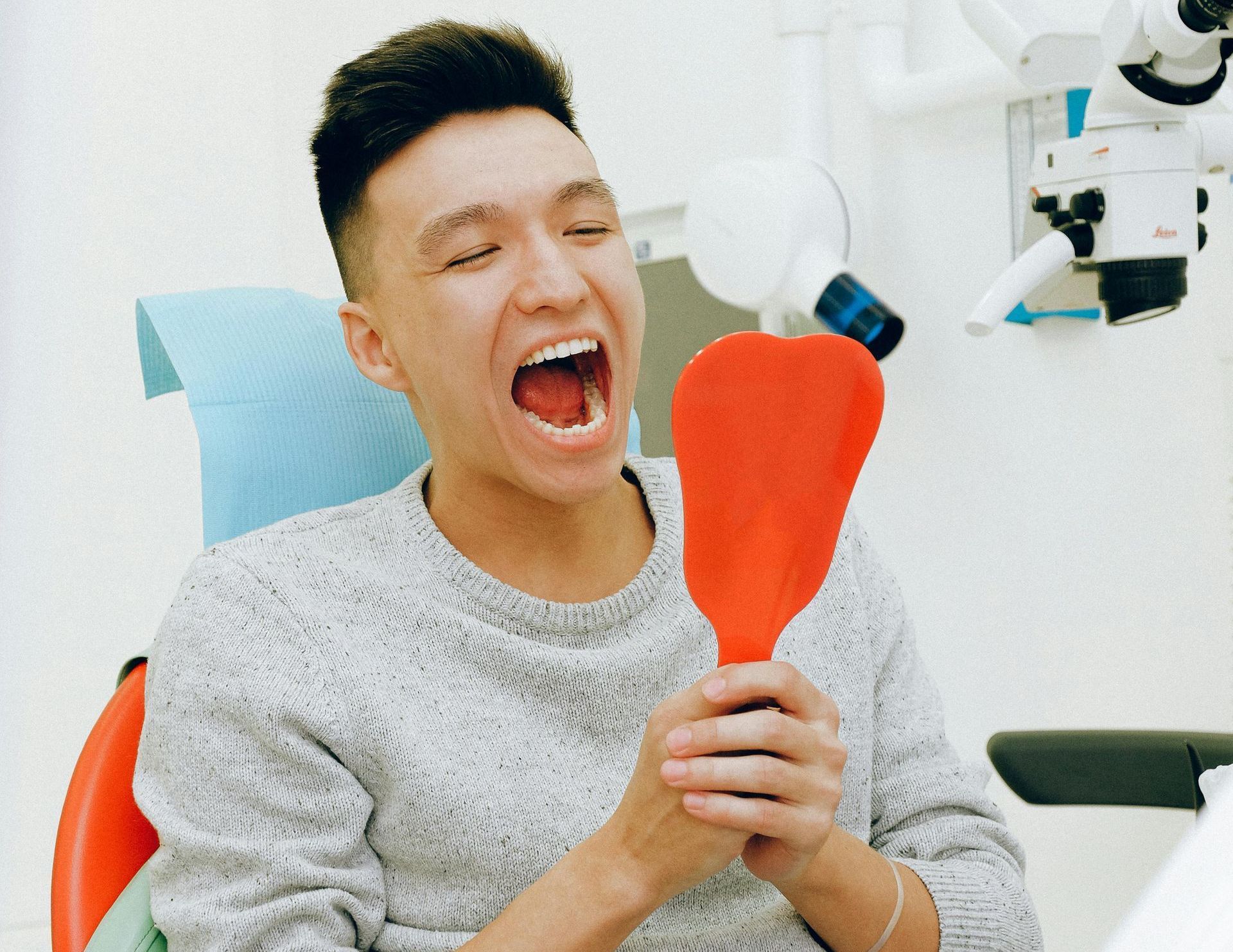 A man is sitting in a dental chair looking at his teeth in a mirror.