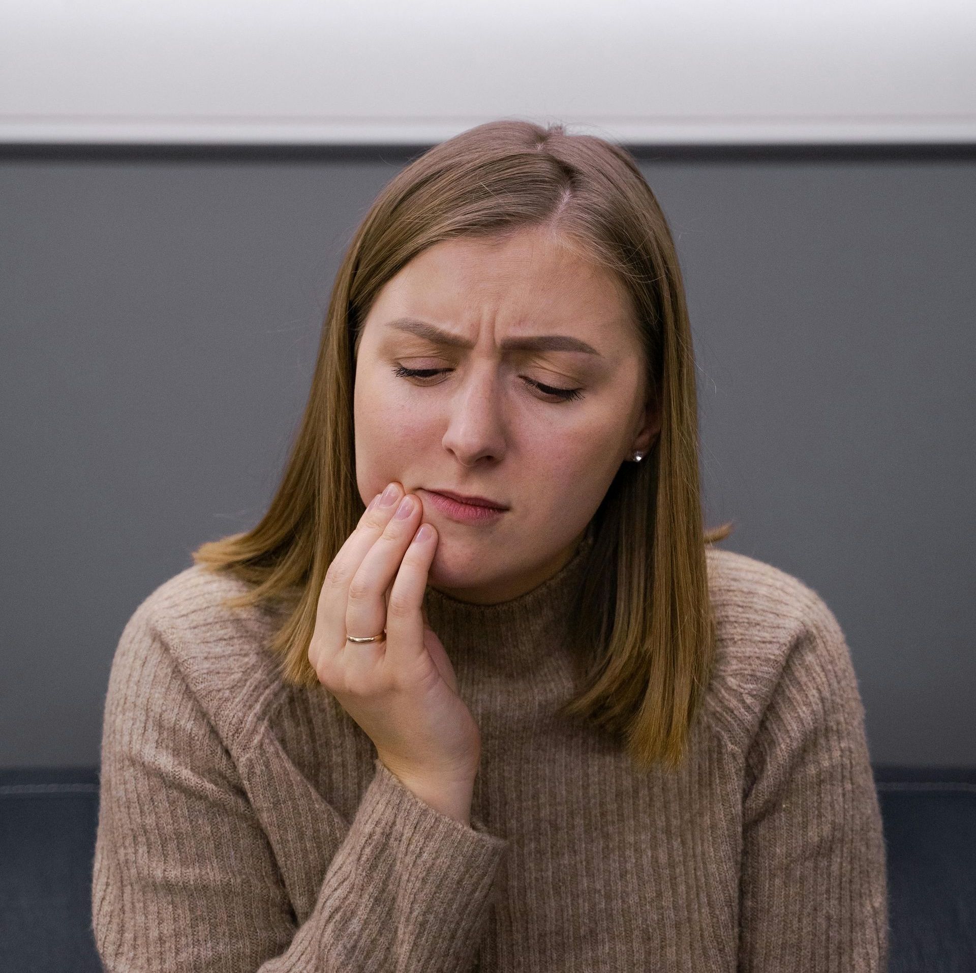 A woman in a brown sweater is holding her hand to her face.