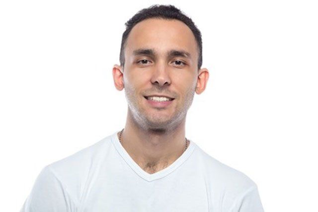 A man in a white t-shirt is smiling and looking at the camera.