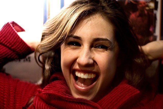 A woman in a red sweater is laughing with her mouth open.