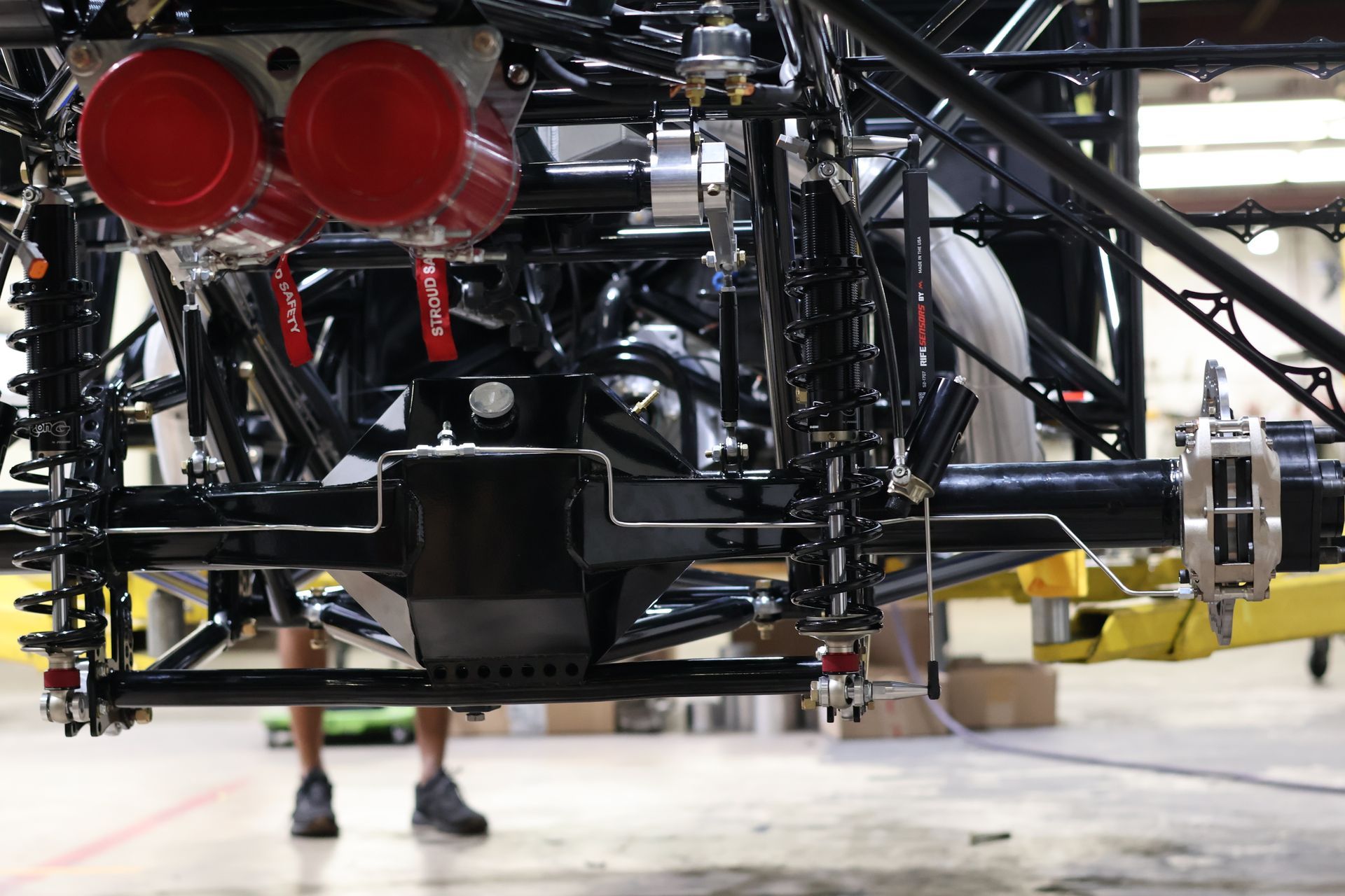 Rear view of a racing car chassis with red taillights and exposed suspension in a garage