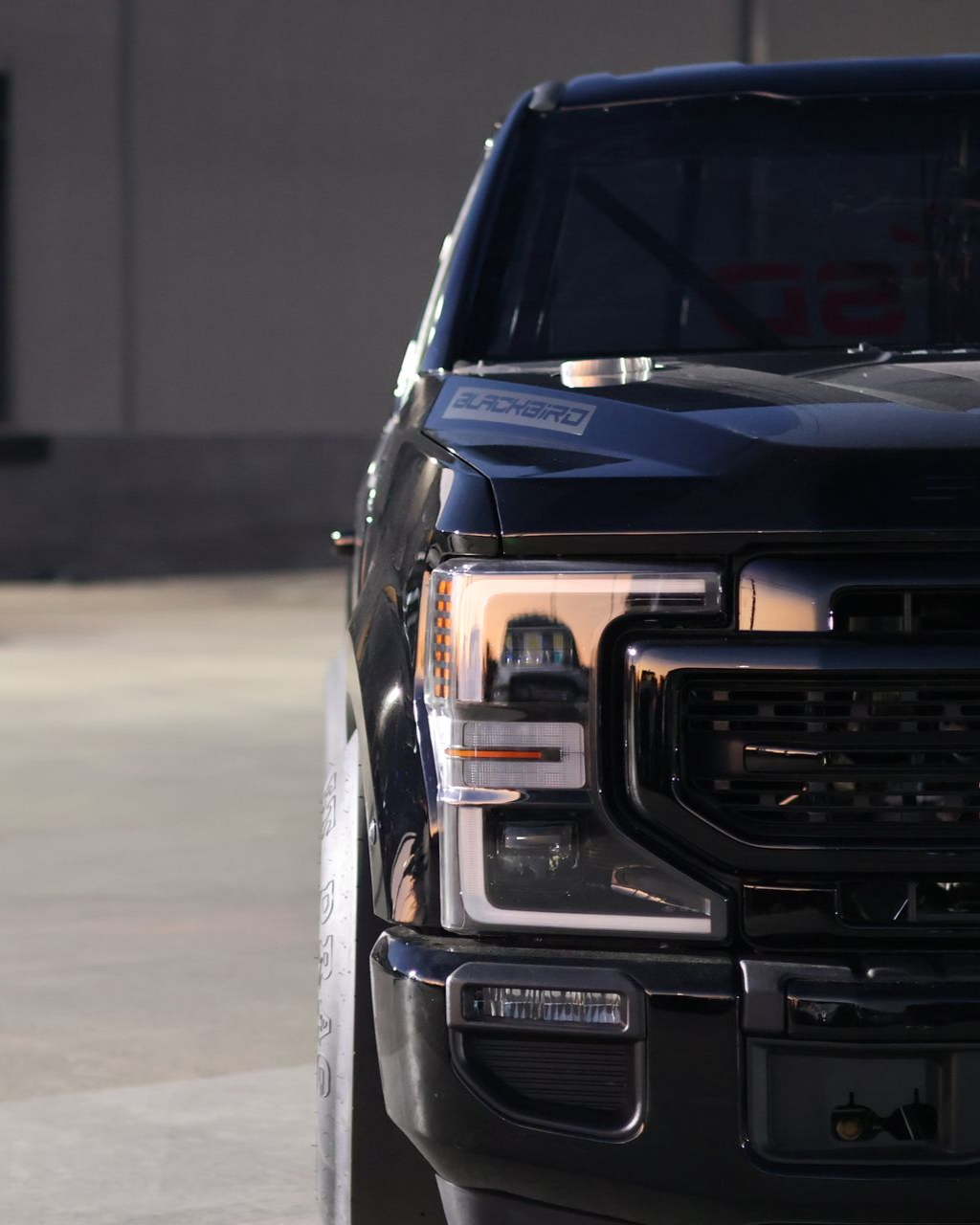 Front view of a black pickup truck parked in a garage, with a headlight illuminated