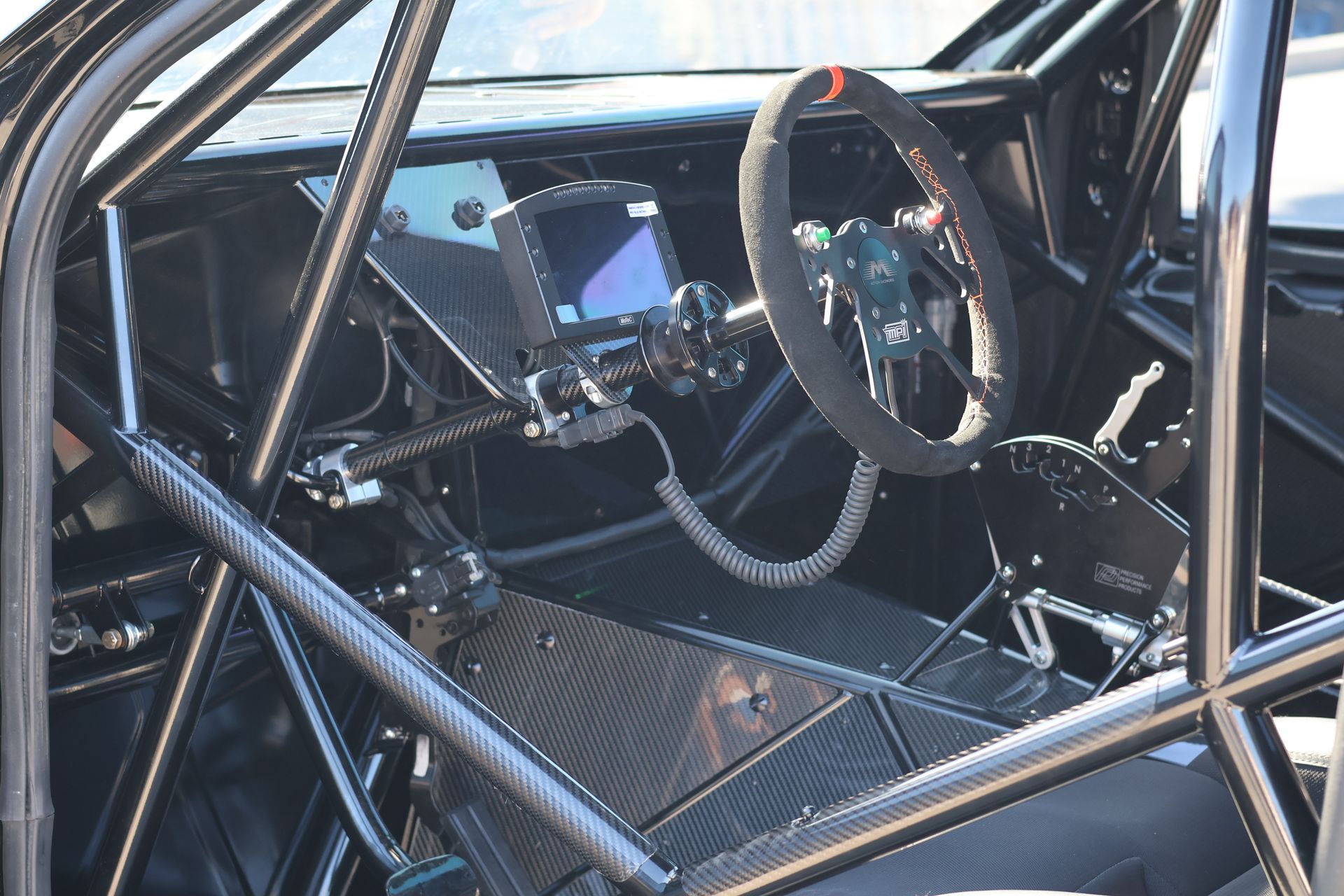 Race car interior with roll cage, steering wheel, and racing seat, viewed through the side window