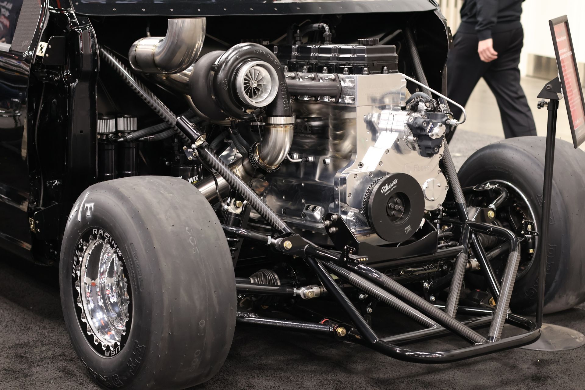 Close-up of a drag racing car’s rear engine and wide slick tires in a pit or garage setting
