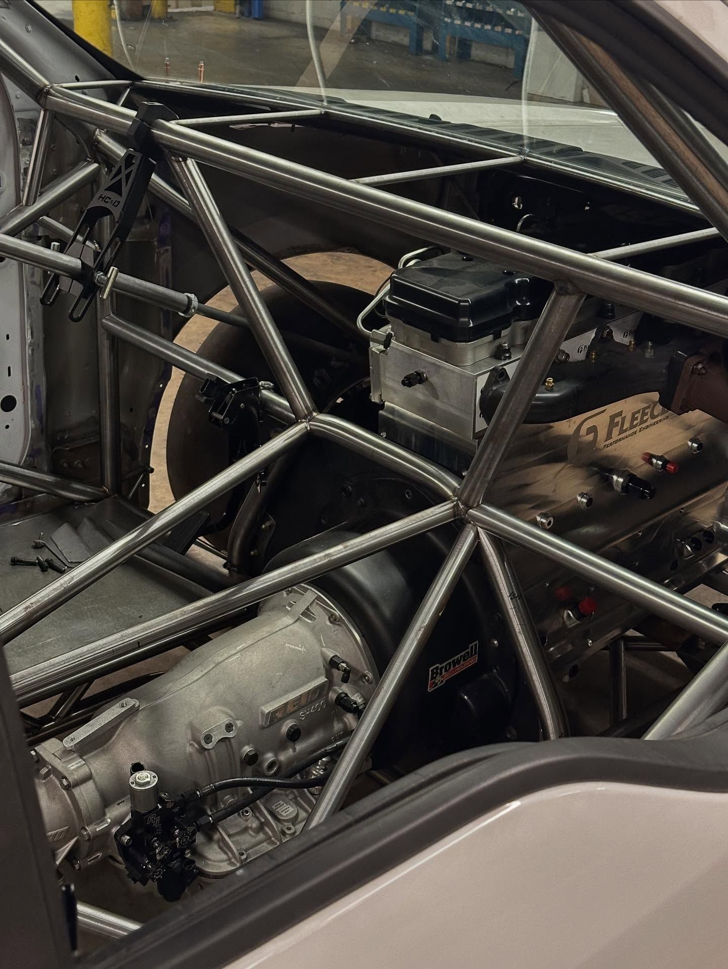 Close-up of a car’s exposed roll cage, engine, and drivetrain inside the chassis.