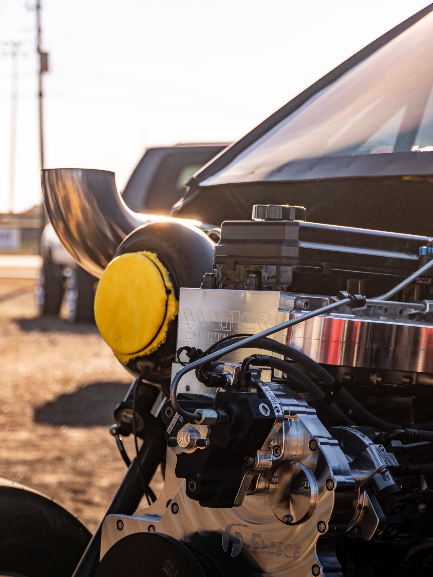 Close-up of a modified car engine with a yellow intake filter and exposed mechanical parts at sunset