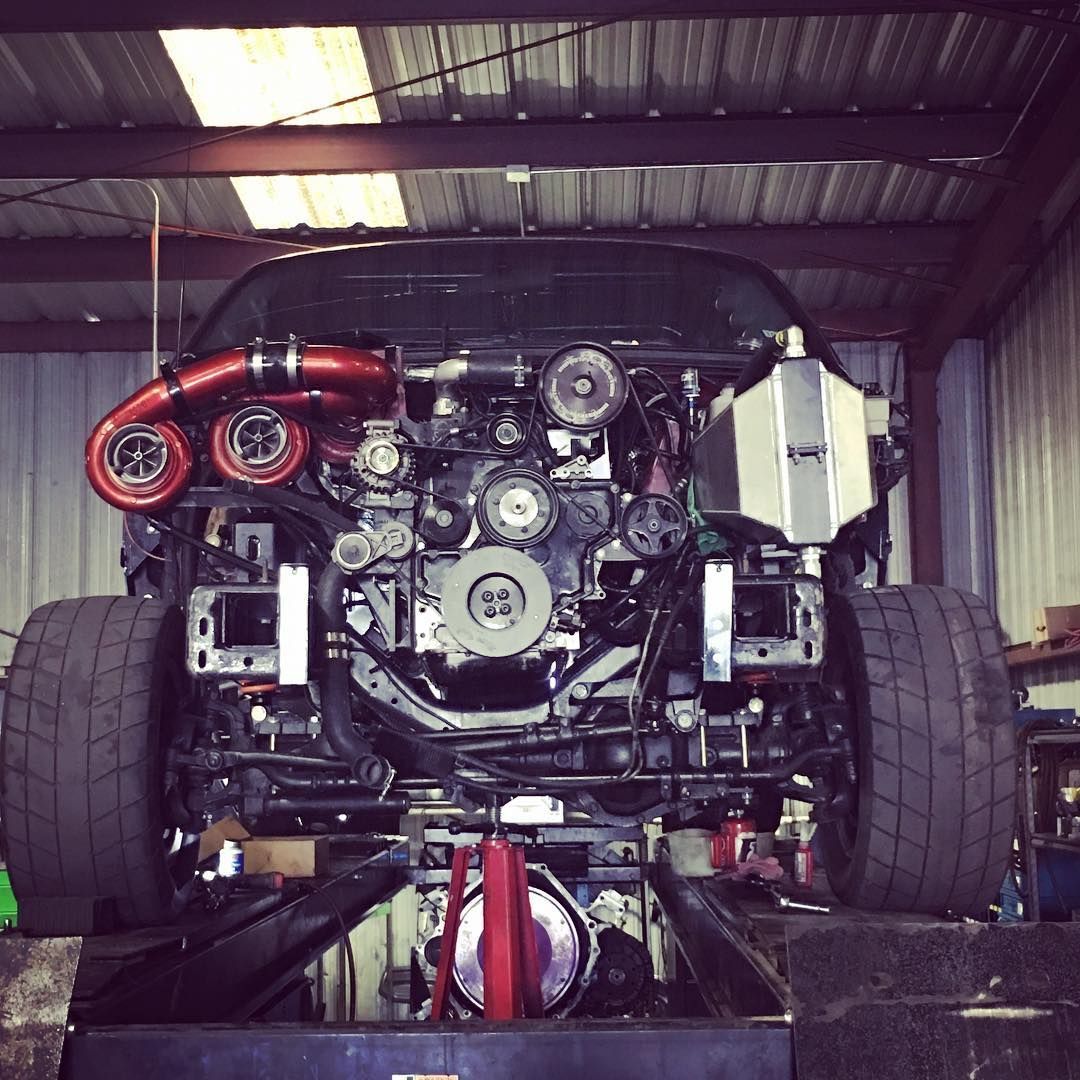 Rear view of a race car’s exposed engine and wide tires in a garage