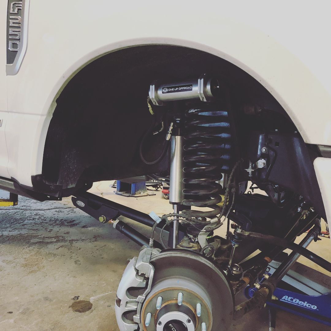 Lifted white truck with exposed front suspension and wheel well at a garage or workshop