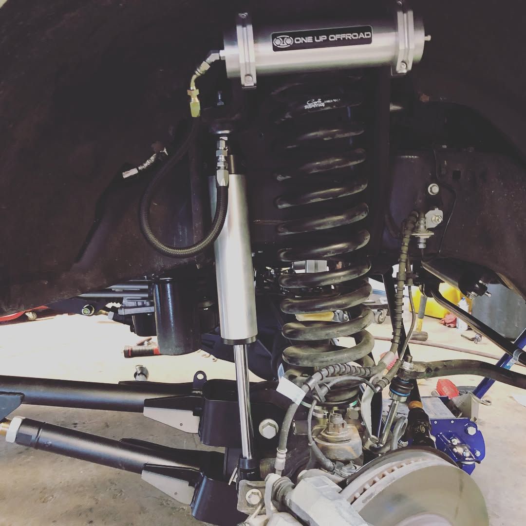 Close-up of a vehicle’s rear suspension with a coil spring, shock absorber, and disc brake assembly.