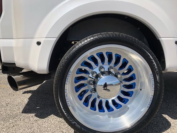 Chrome wheel with blue accents on a white vehicle, shown from the side near the rear wheel arch