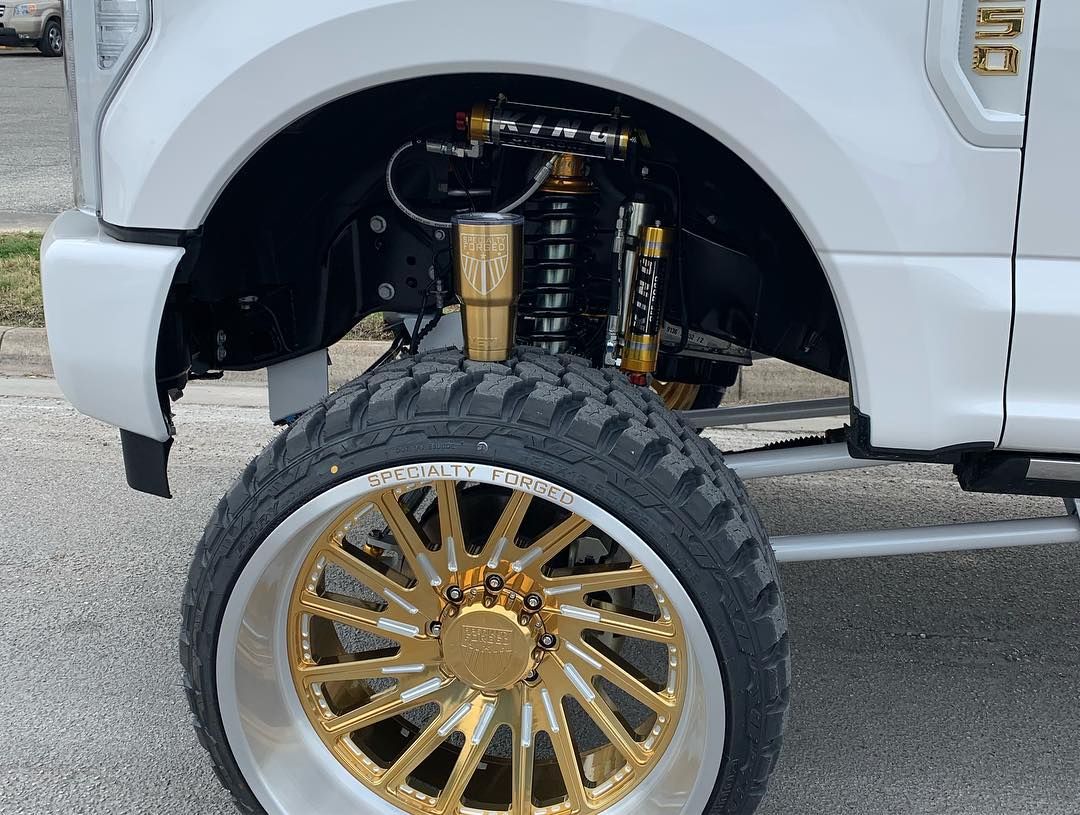 White truck with gold custom wheel and exposed suspension in the front wheel well