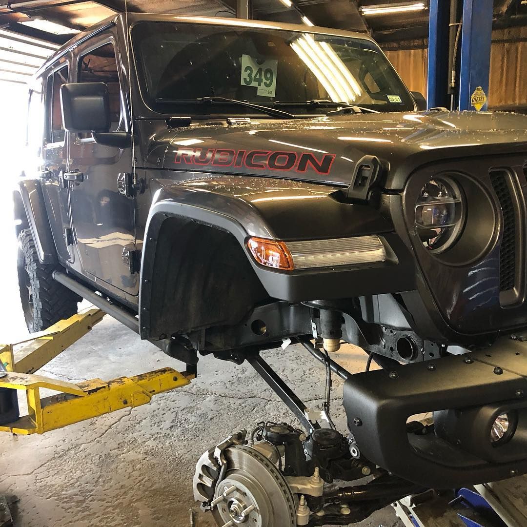 Black Jeep Rubicon on a lift in an auto shop, with front wheel removed during repair