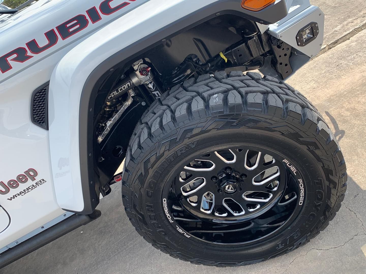 Close-up of a white Jeep Rubicon with large off-road tire and black wheel on pavement