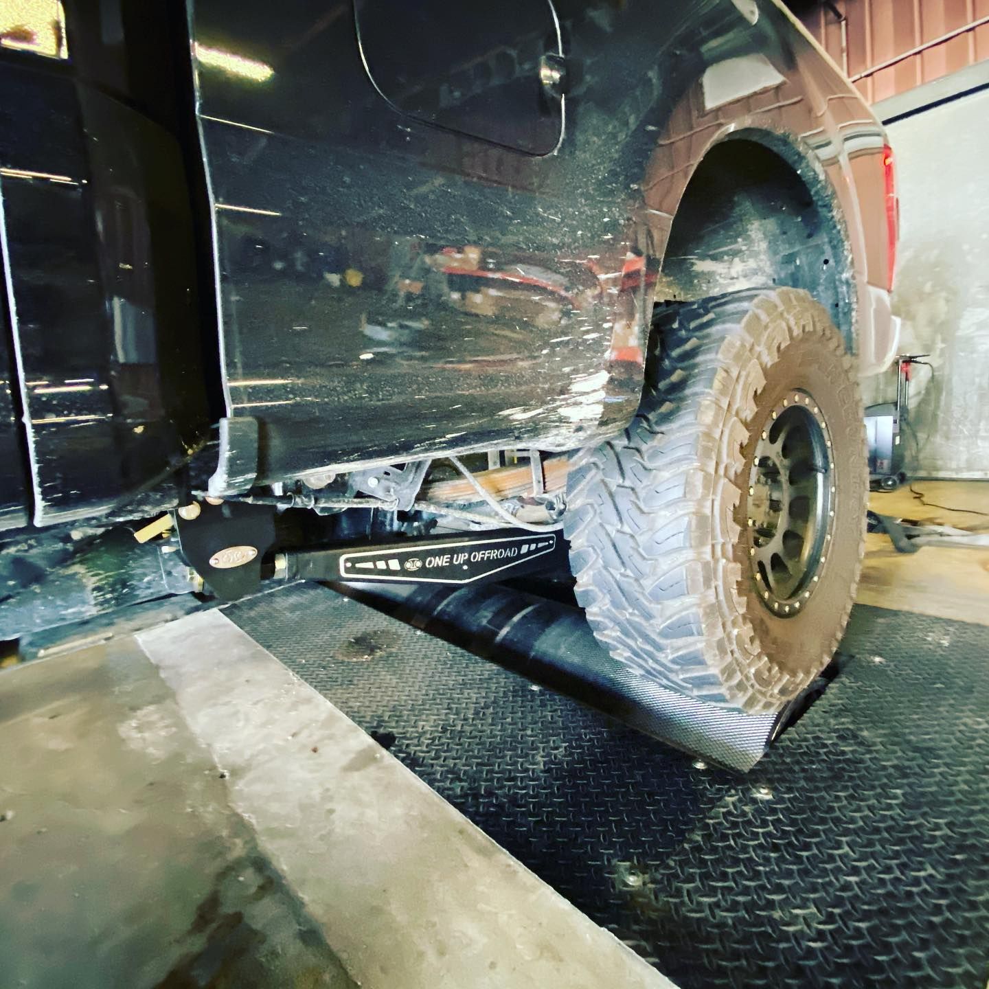 Black pickup truck on a lift in a repair shop, showing a rear tire and damaged side panel.