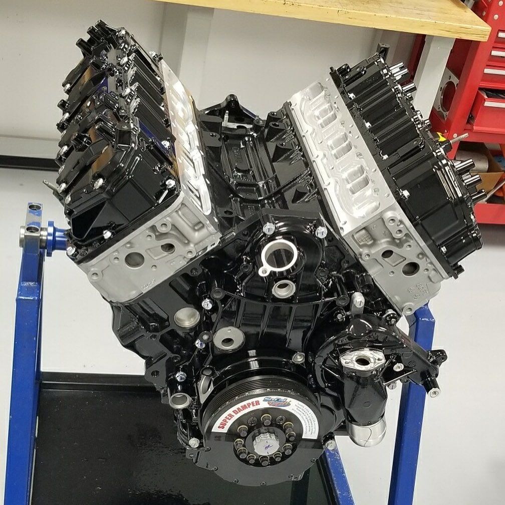 Black V8 engine on a stand in a workshop, with silver cylinder heads and exposed pulleys