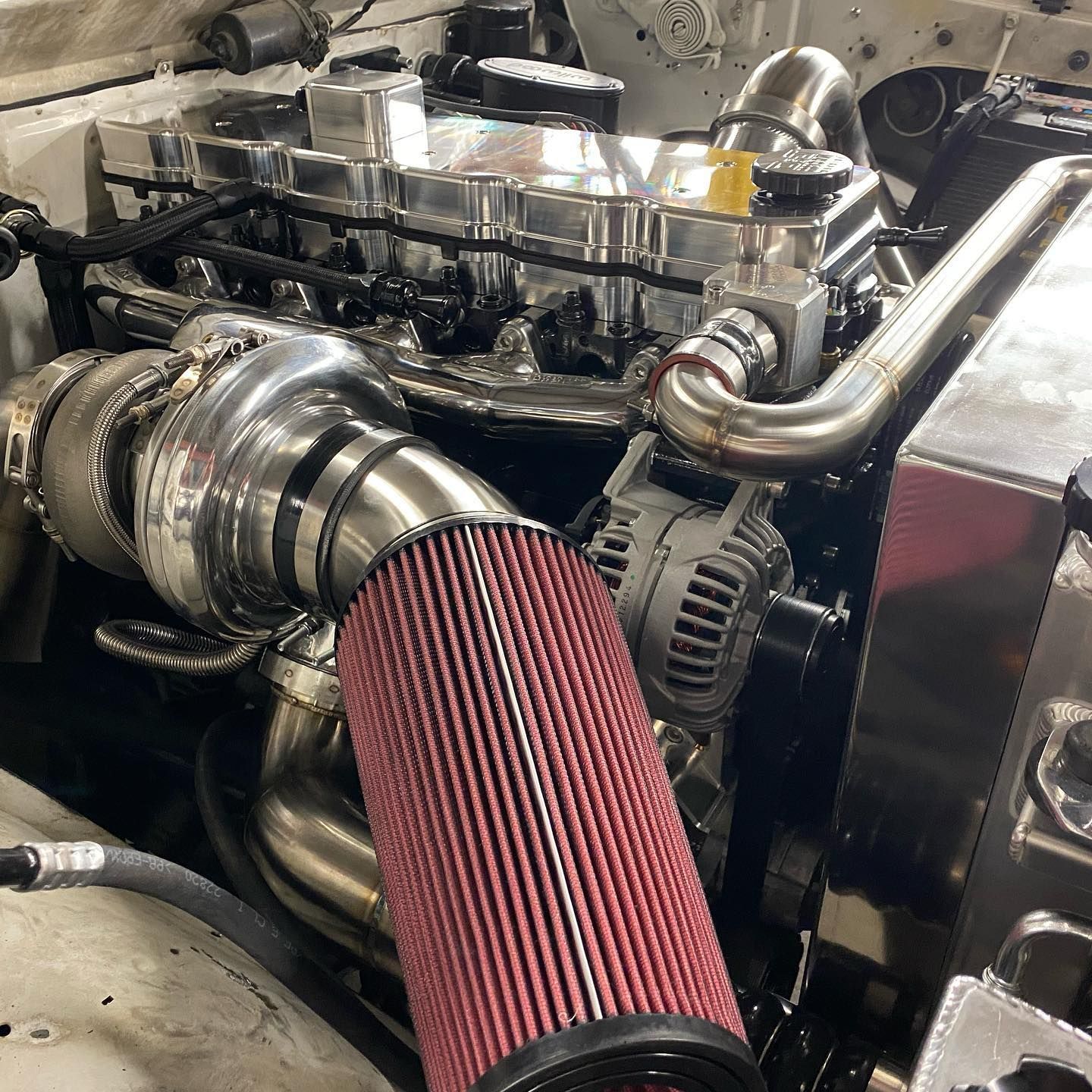 Close-up of a car engine bay with a red cone air filter and polished turbo piping.