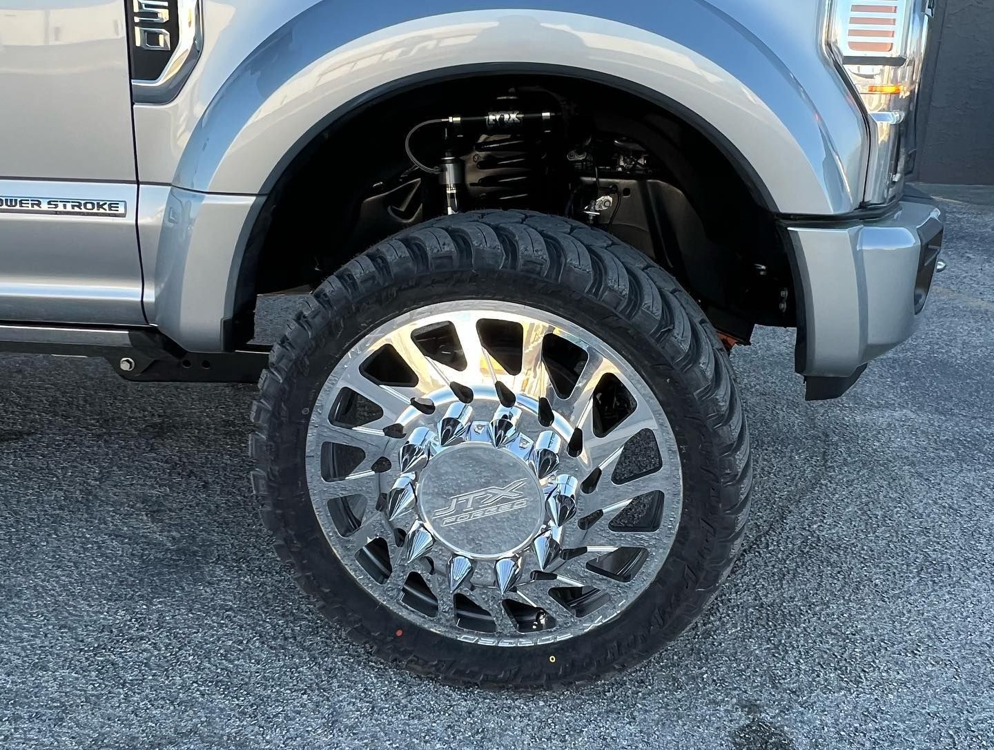 Silver pickup truck close-up showing a large chrome wheel and rugged off-road tire.