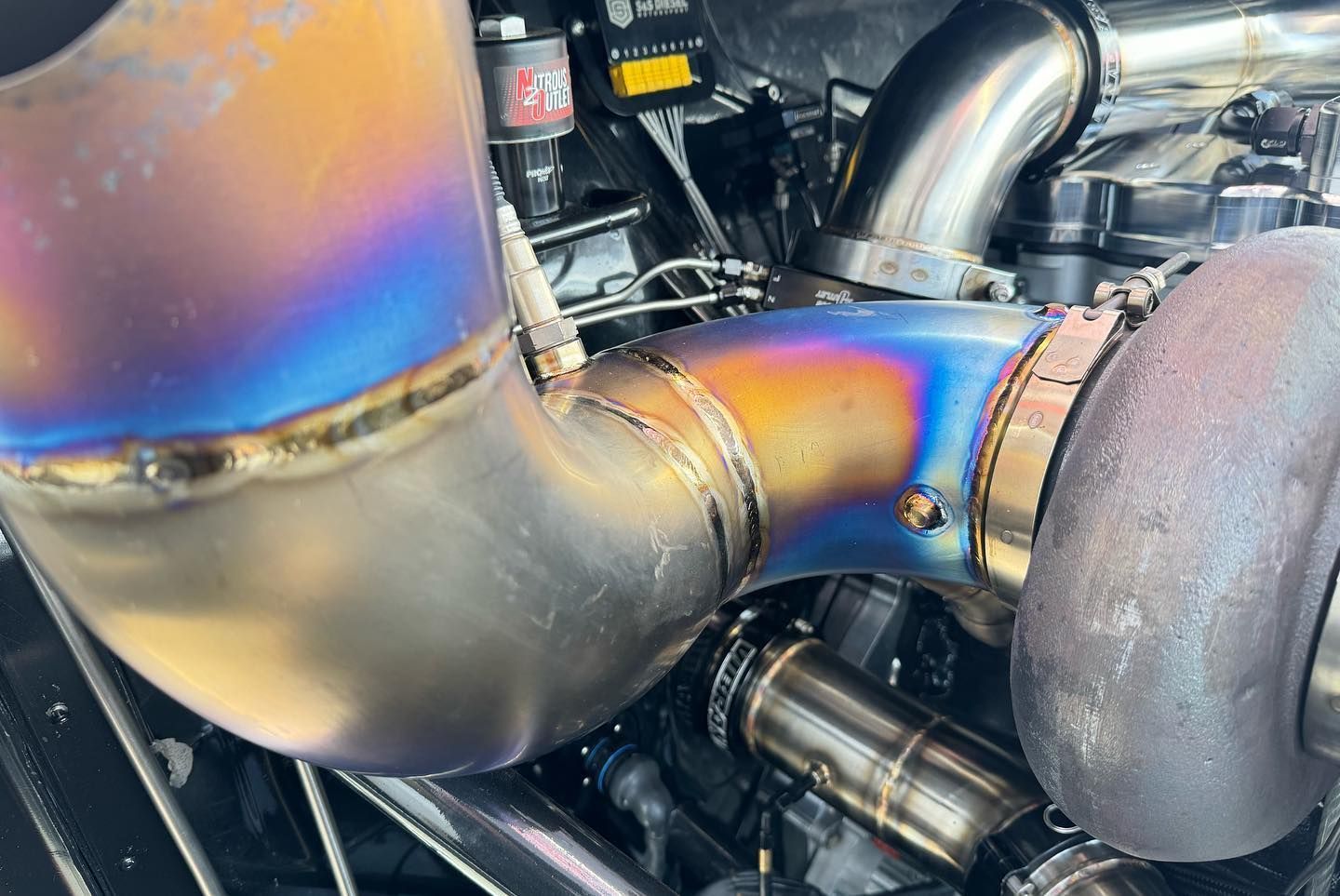 Close-up of iridescent welded exhaust pipes with a turbocharger in an engine bay