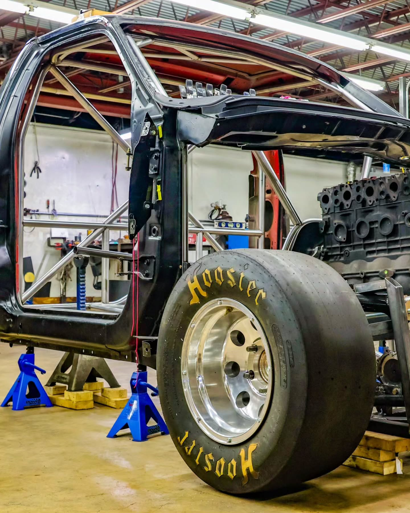 Race car chassis on jack stands in a workshop with a large rear tire and exposed engine.