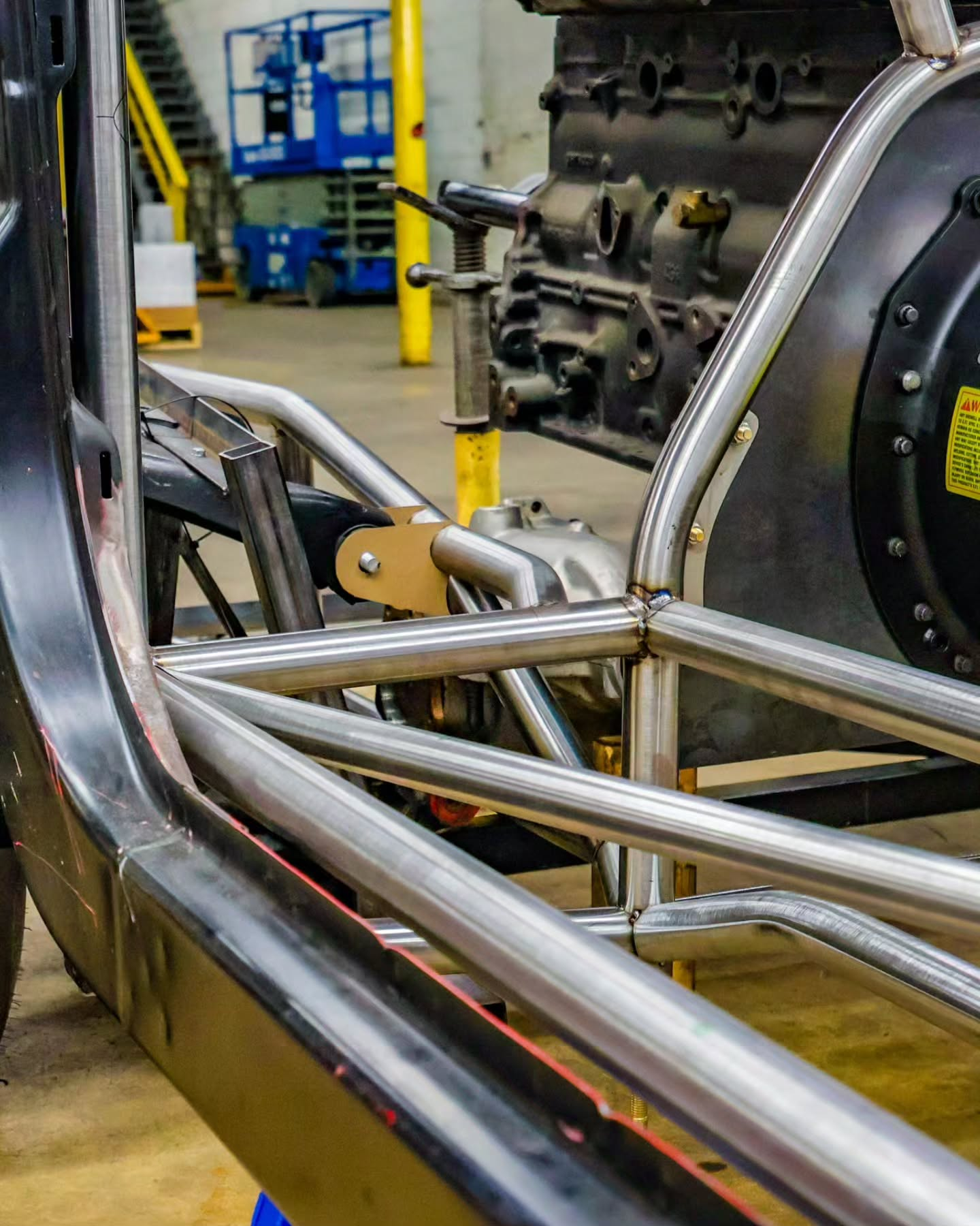 Metal tubing and machinery in an industrial workshop, with a vehicle frame in the foreground