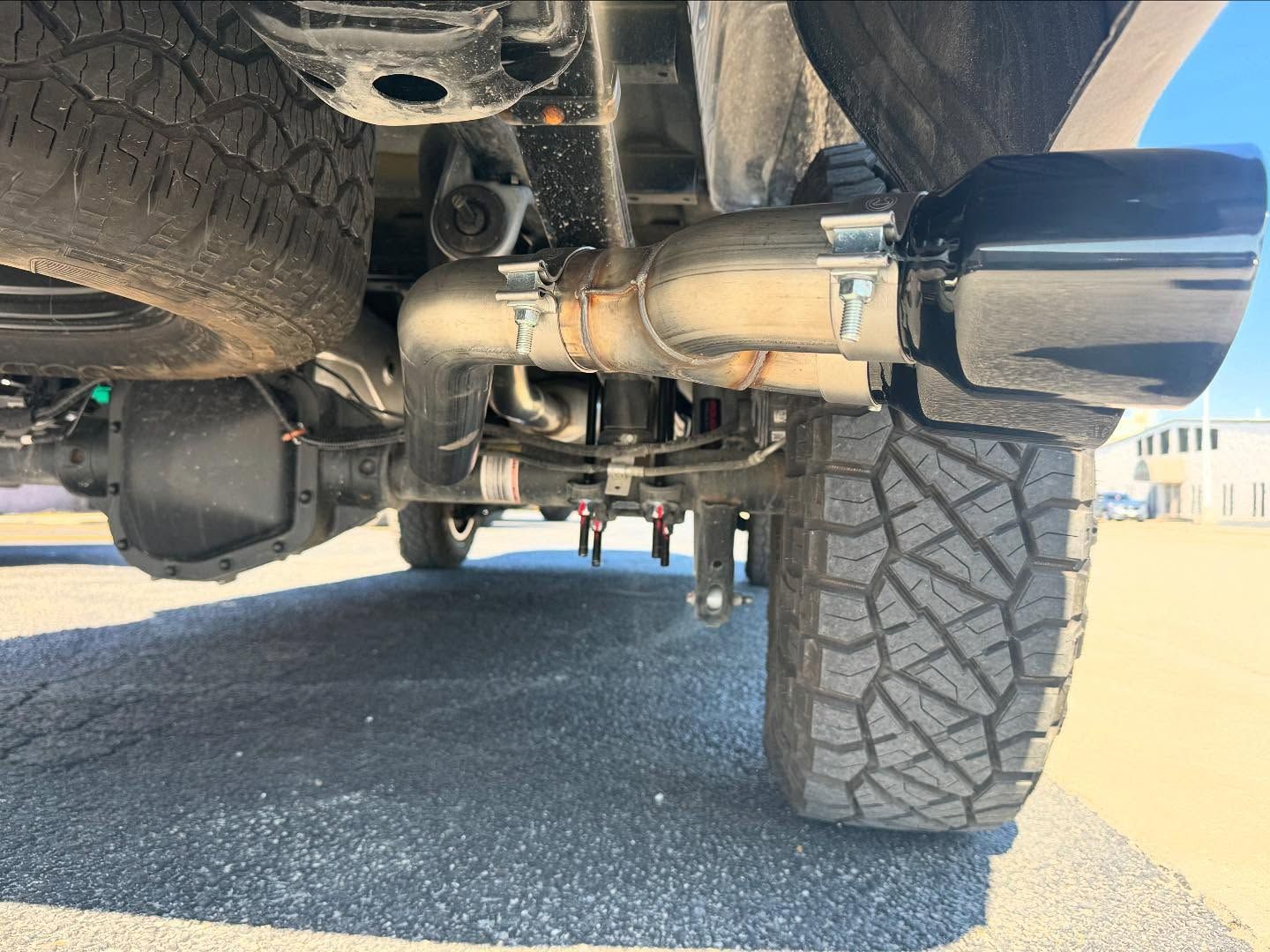 Undercarriage view of a lifted truck, showing exhaust, suspension, and a large off-road tire