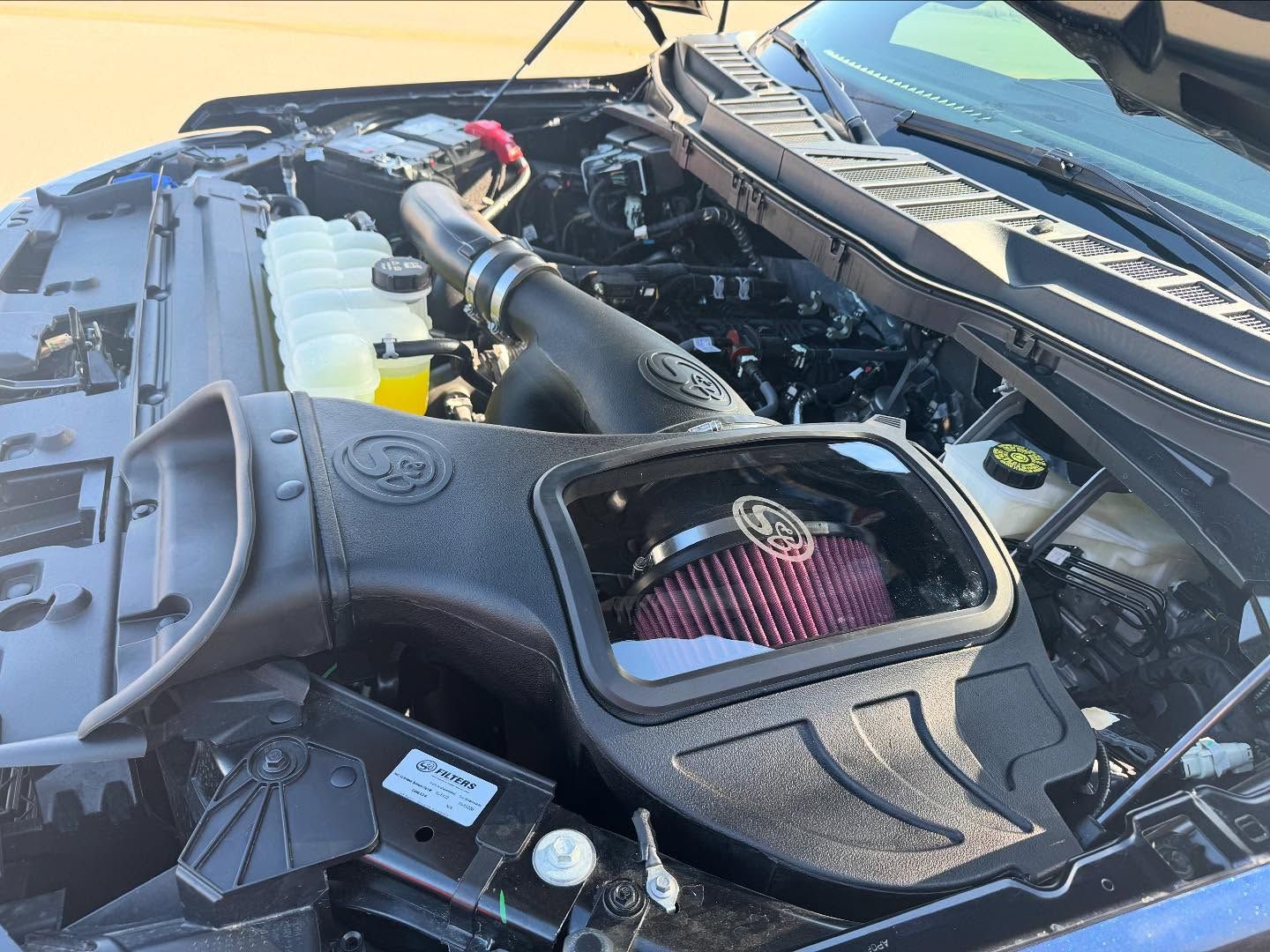 Open car engine bay with black air intake cover and red cone filter under the hood