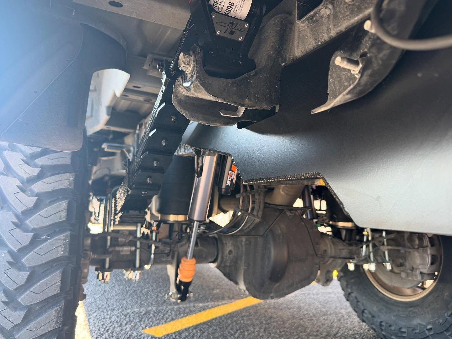 Undercarriage of a lifted off-road truck showing suspension, axle, and large tires on pavement
