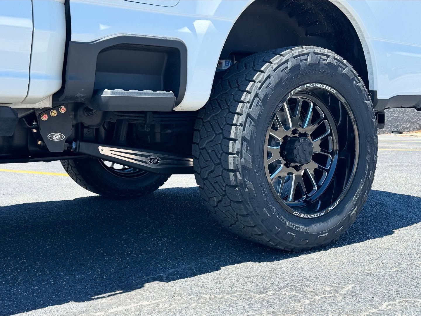 White pickup truck with black off-road wheel parked on pavement in bright sunlight
