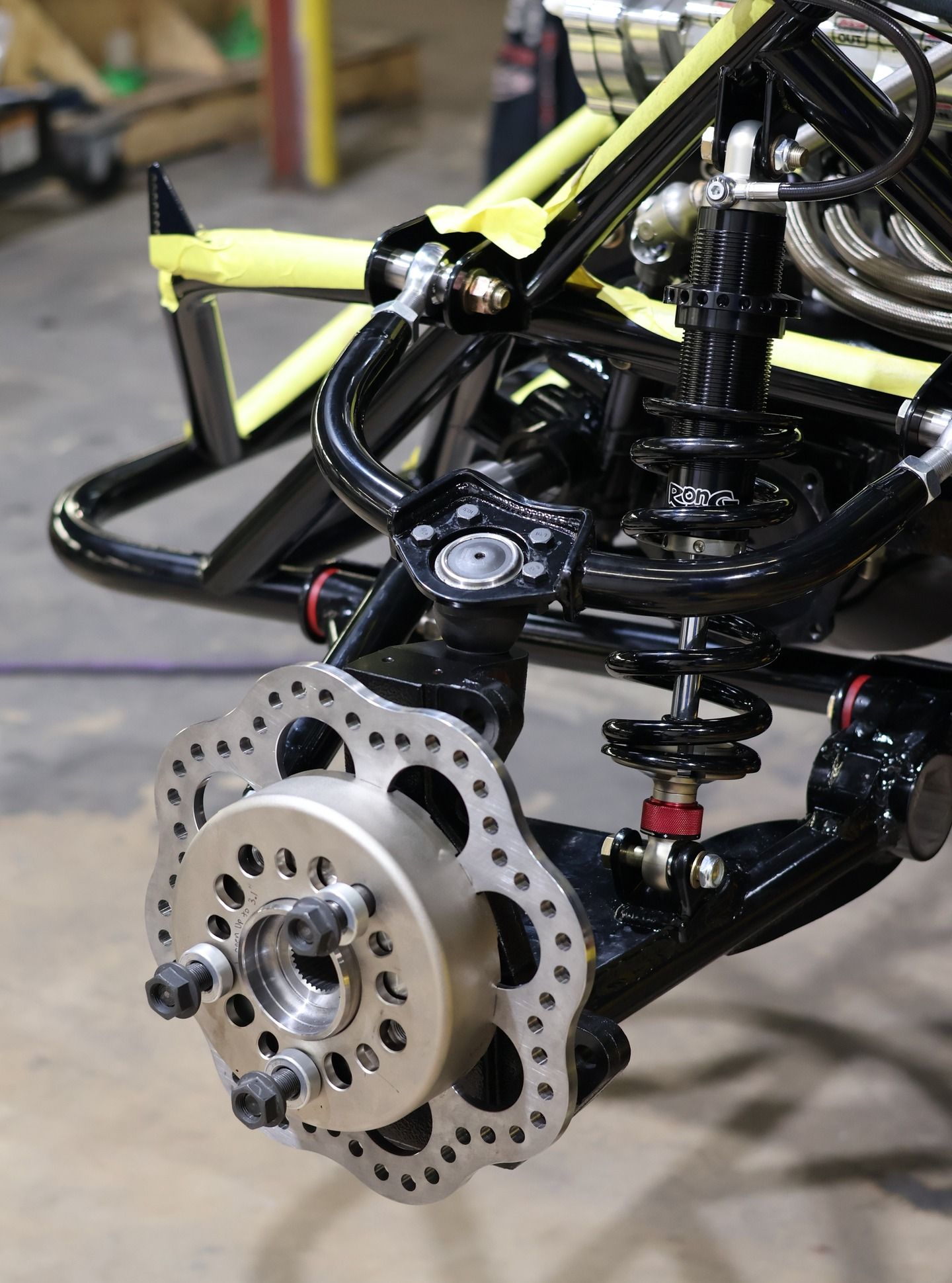 Close-up of a go-kart rear wheel assembly with brake disc and suspension parts in a workshop.