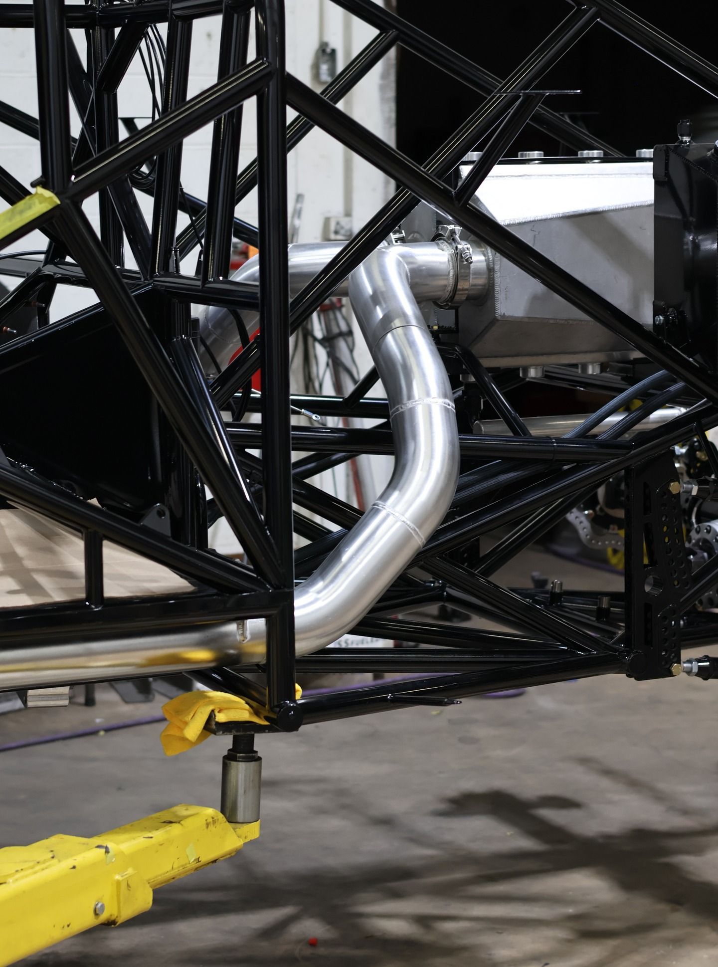 Yellow tow bar attached to a black race car chassis with silver exhaust pipes in a garage