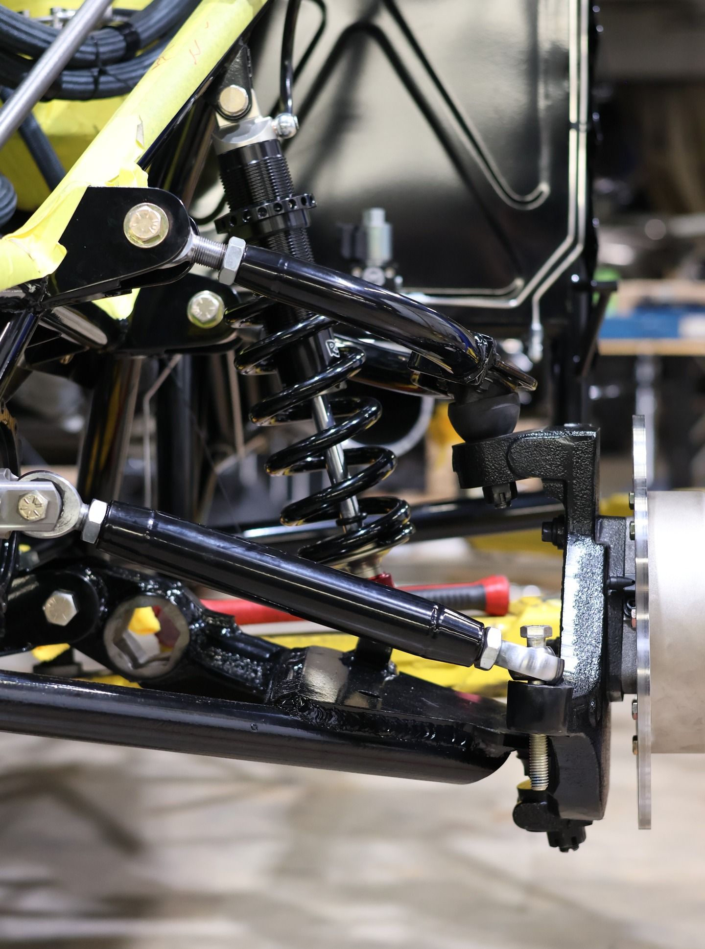 Close-up of a race car’s suspension and front wheel assembly in a garage.