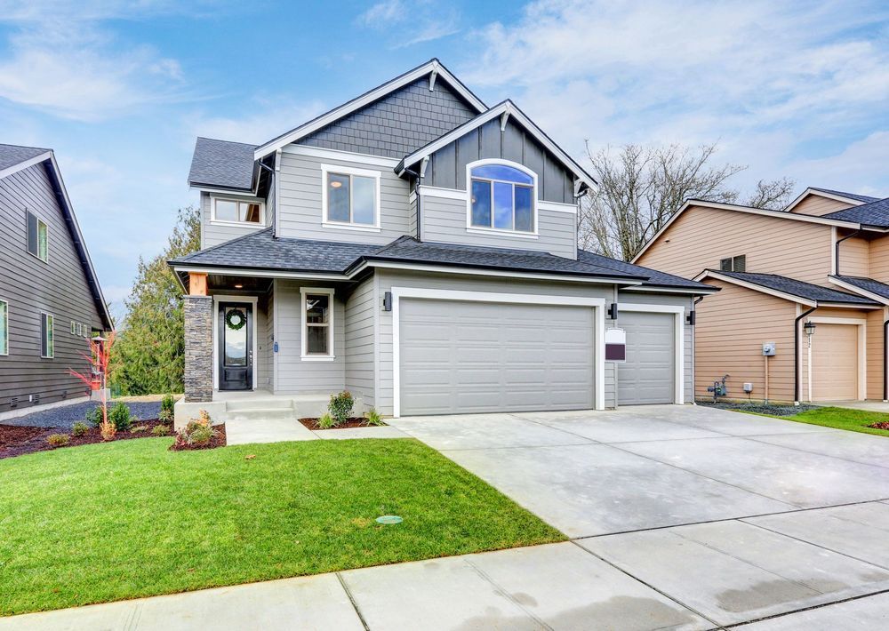 Two-story gray house with garage, blue sky, and green lawn.