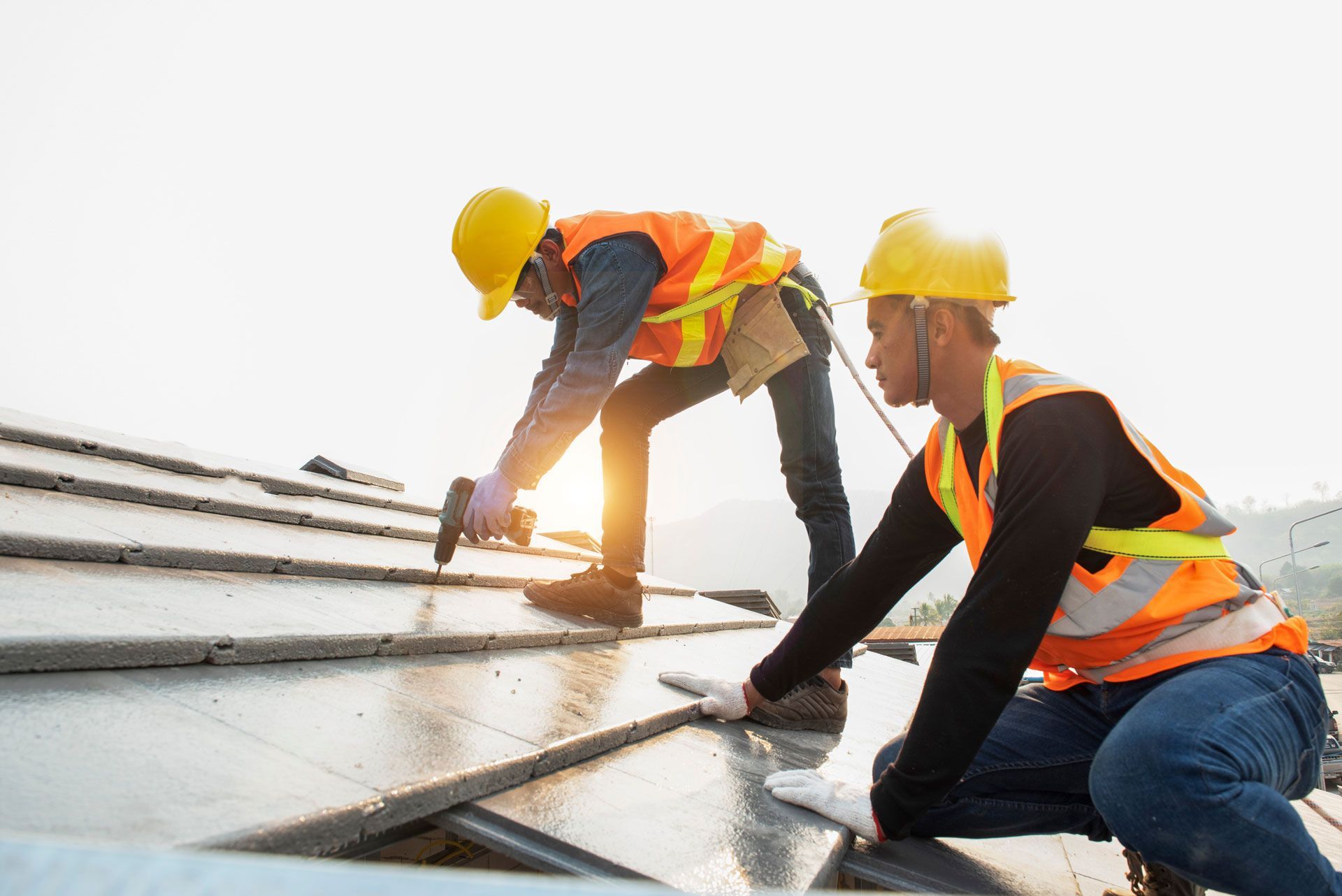 Two workers in hard hats and vests installing solar panels on a rooftop in sunlight.