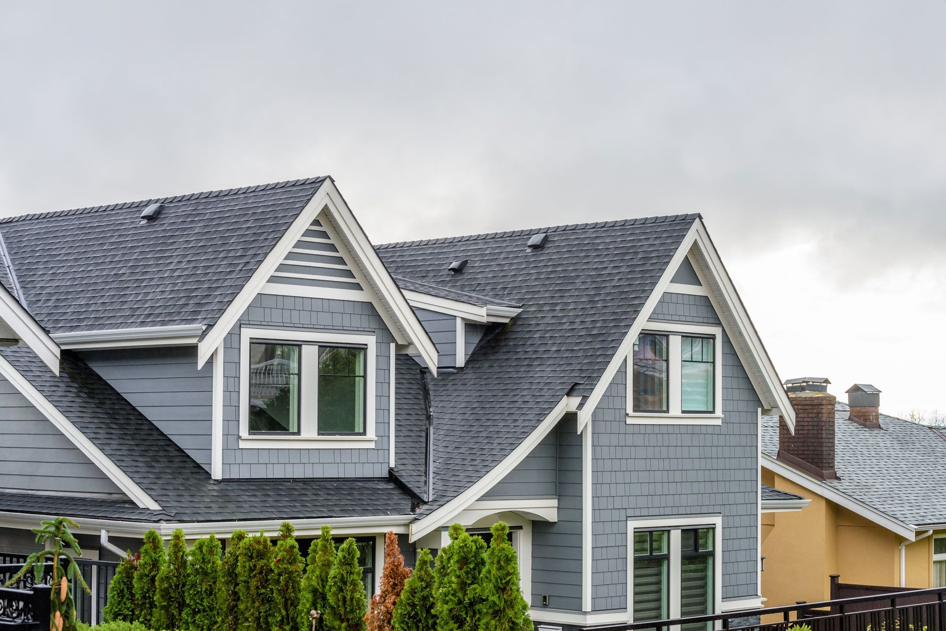 Gray houses with dark gray roofs, windows, and green bushes. Overcast sky.